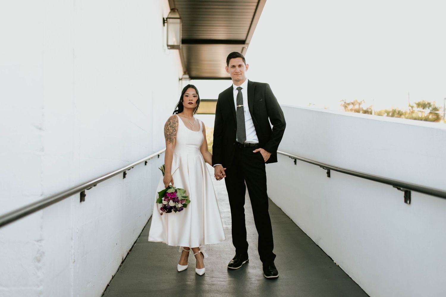 Bride and groom holding hands walking on modern outdoor walkway after wedding ceremony at the Urban Stillhouse.