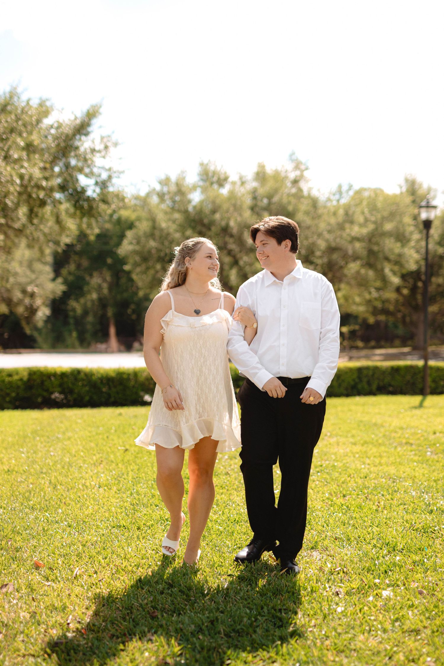Happy couple walking hand in hand across a sunny green lawn, smiling at each other.