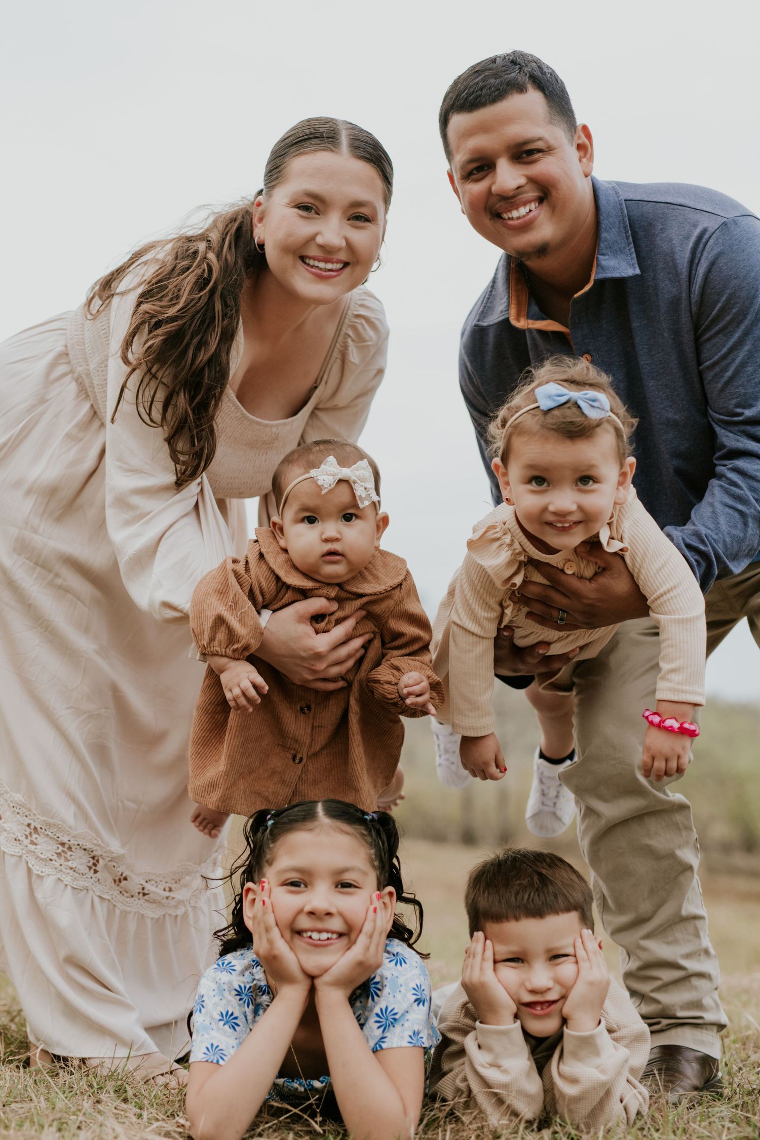 Happy family of six poses together outdoors with two parents and four young children.