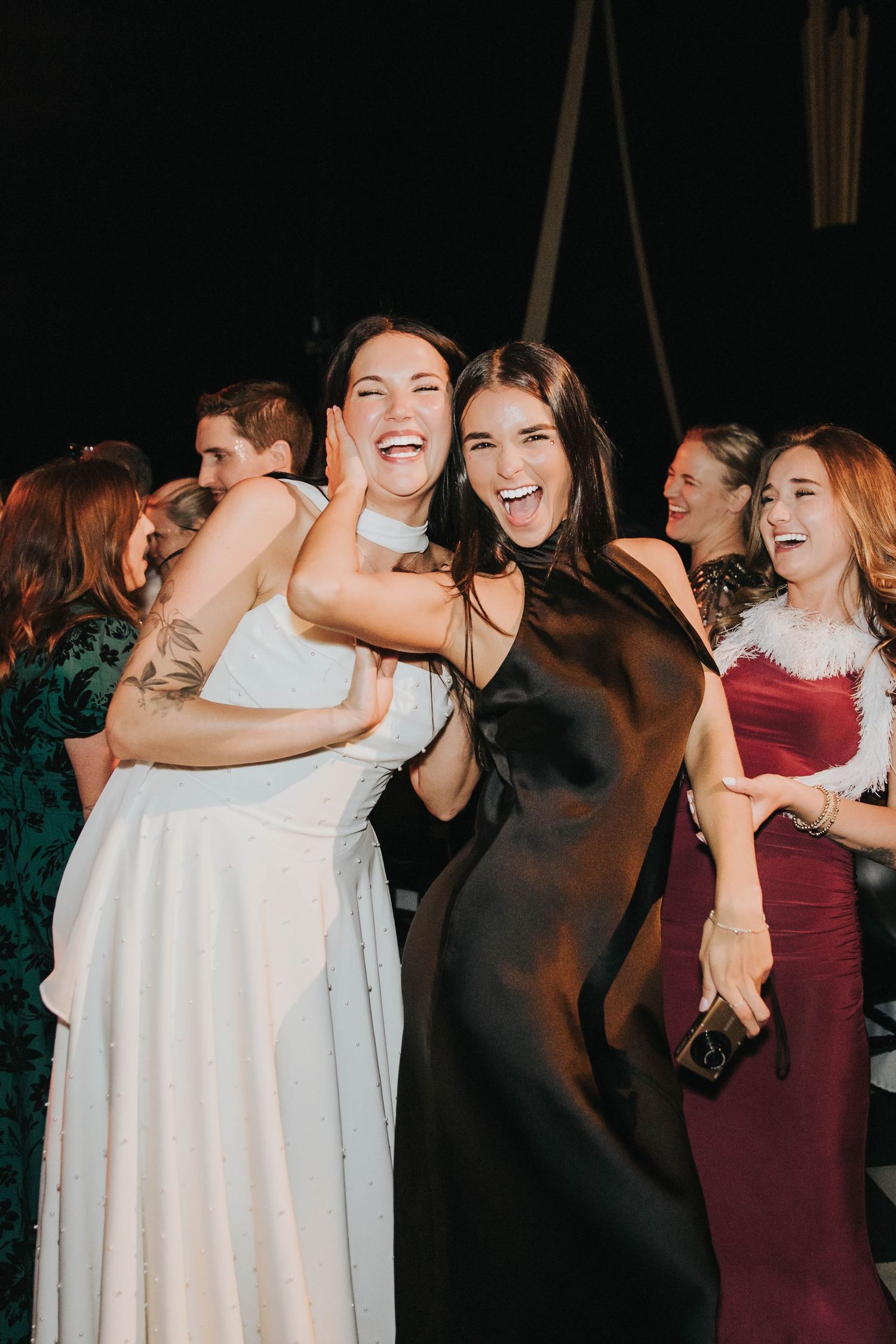 Bride in white gown joyfully hugging a guest in black dress while celebrating at a lively wedding reception at the Floridian Social.