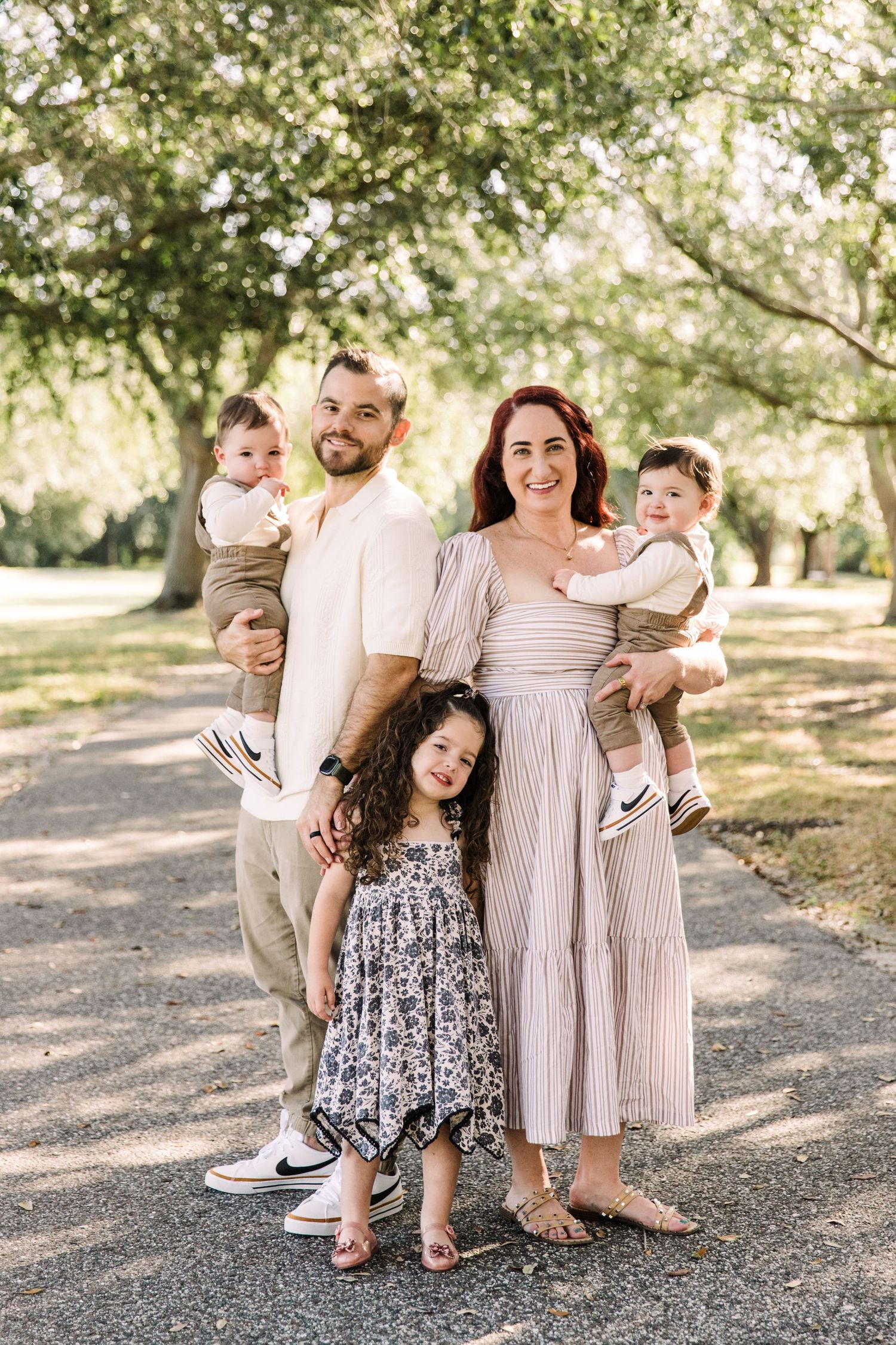 Family portrait with parents holding twin babies and young daughter in sunny park at Cypress Pointe Park.