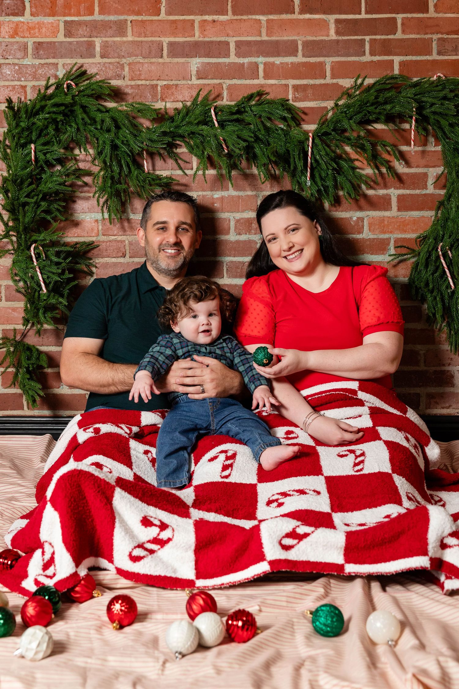 Family with baby boy sitting on bed with candy cane quilt and Christmas decorations.