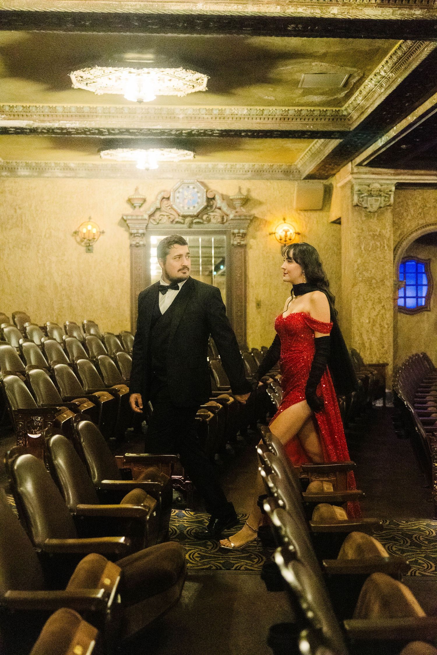 Man in tuxedo and woman in red dress walking through ornate vintage Tampa theater interior.