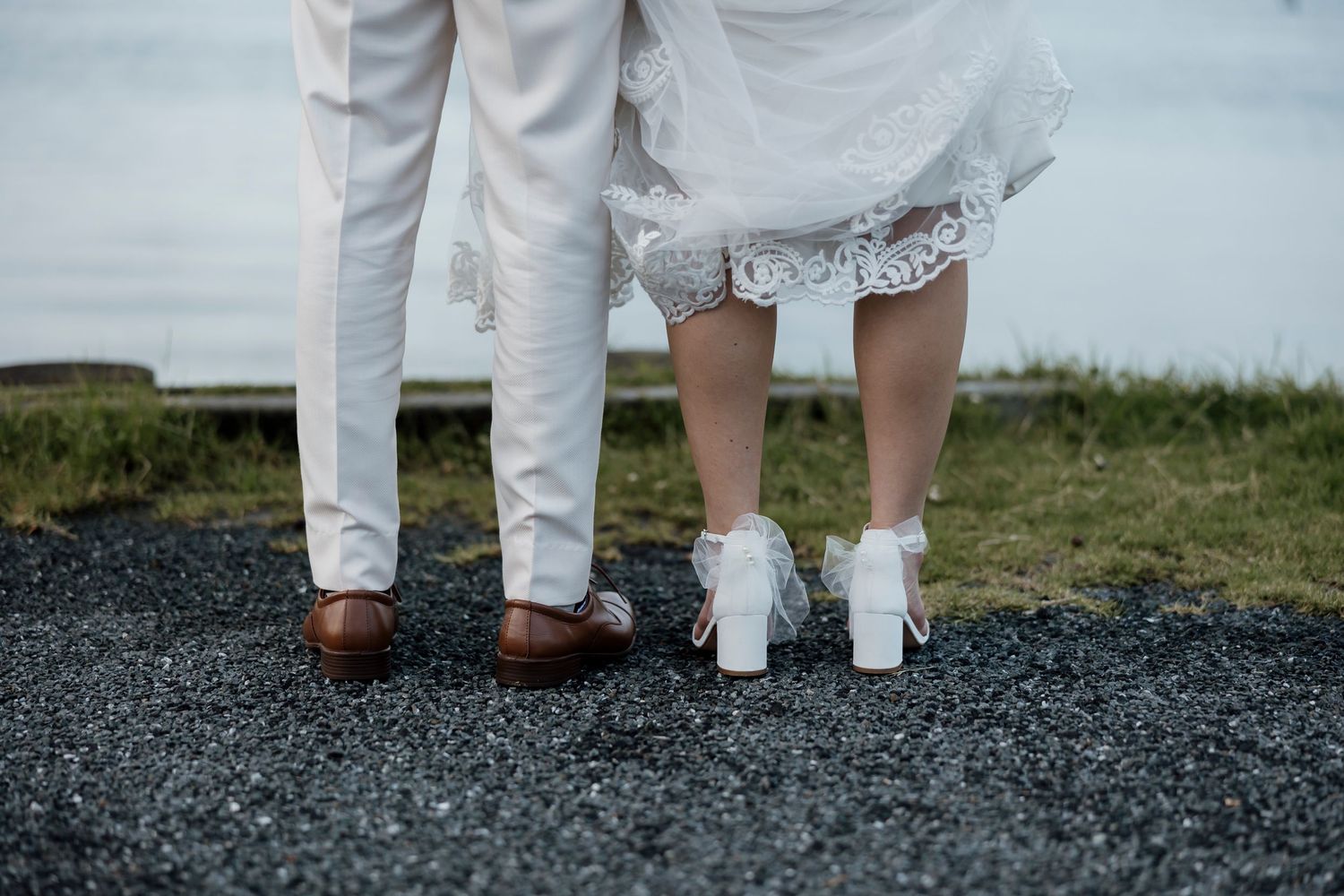 Detail shot of bride in white heels with tulle bows and groom in tan leather shoes walking together — Oh Joy! Photography Tauranga