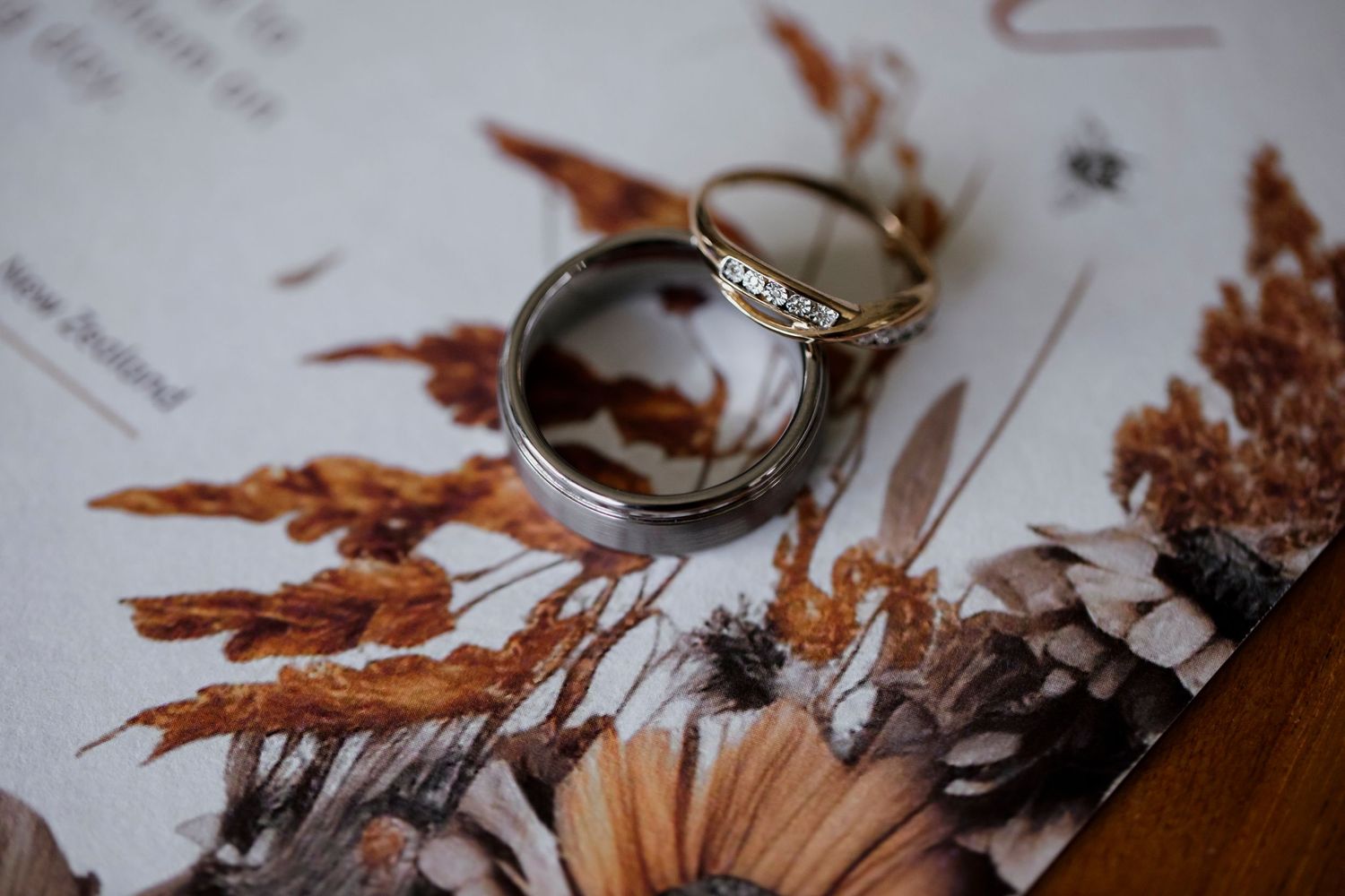 Close-up of wedding rings resting on a floral wedding invitation — Oh Joy! Photography Tauranga