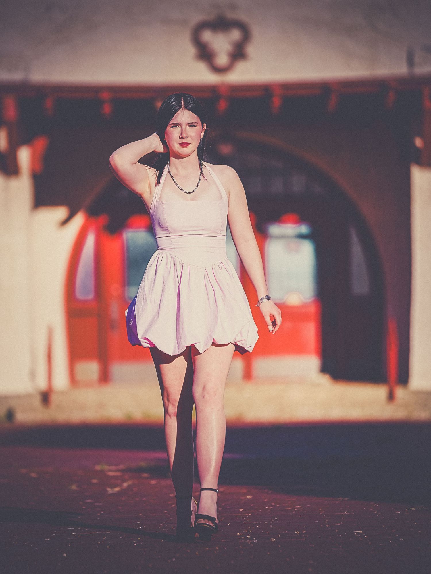 Young woman in white bubble dress posing confidently before red arched building facade.