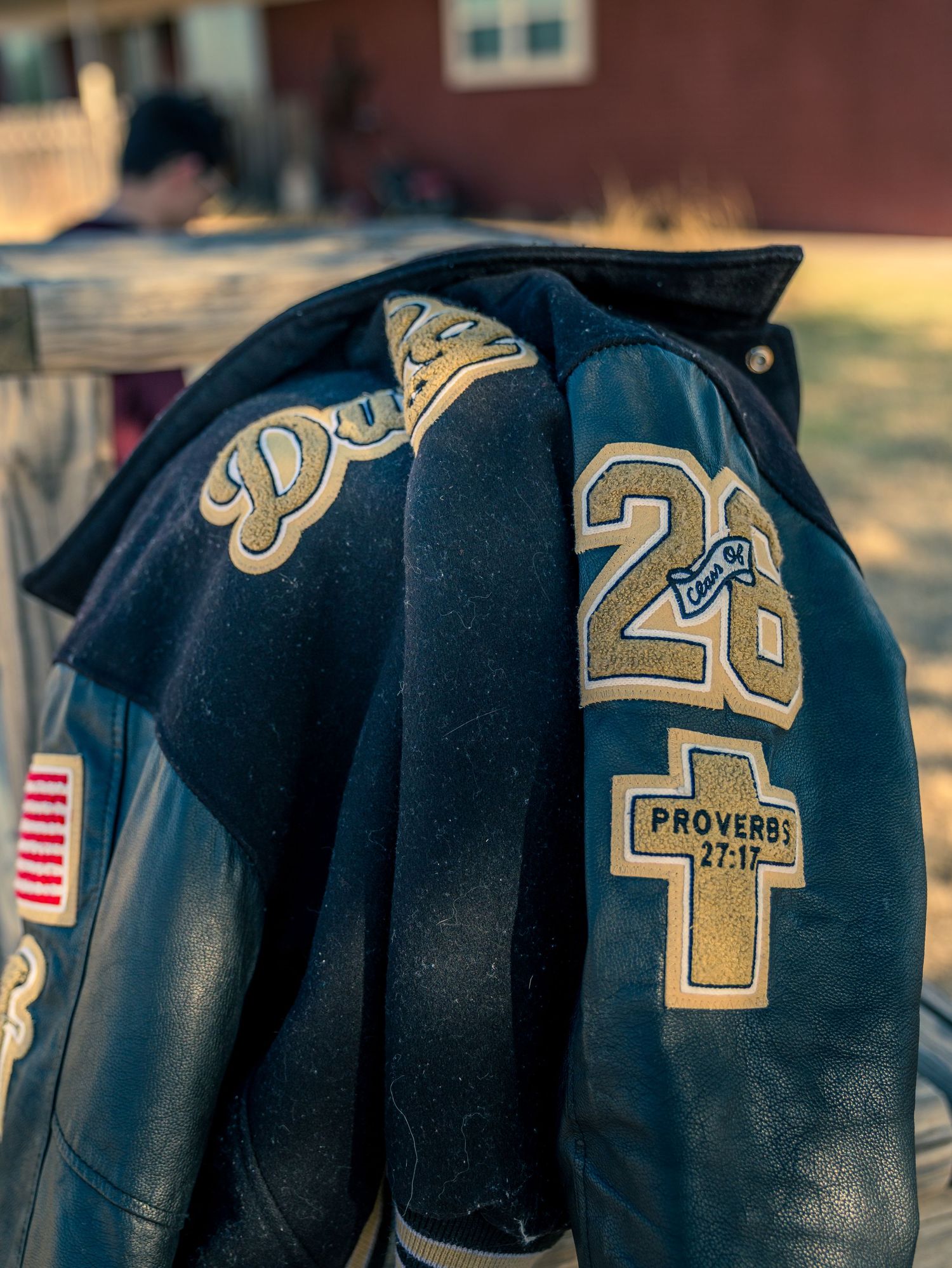 Close-up of a varsity letterman jacket with Proverbs 27:17 cross patch and American flag emblem.