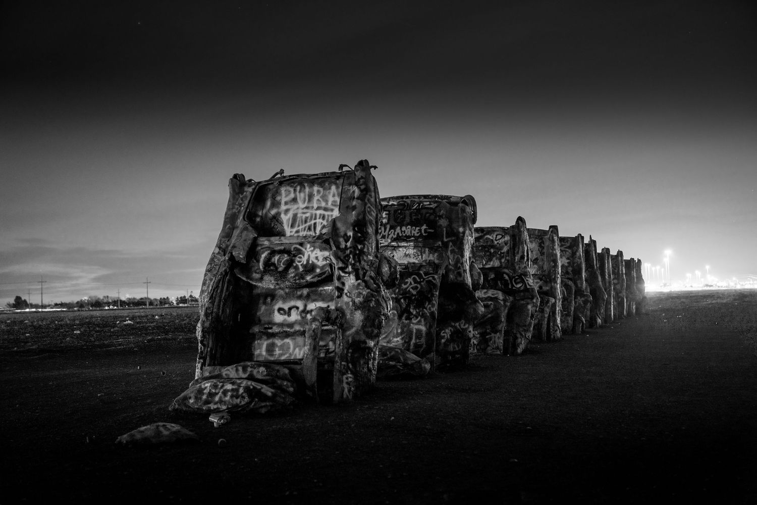 Black and white close-up of graffiti-covered Cadillacs at Cadillac Ranch at night.