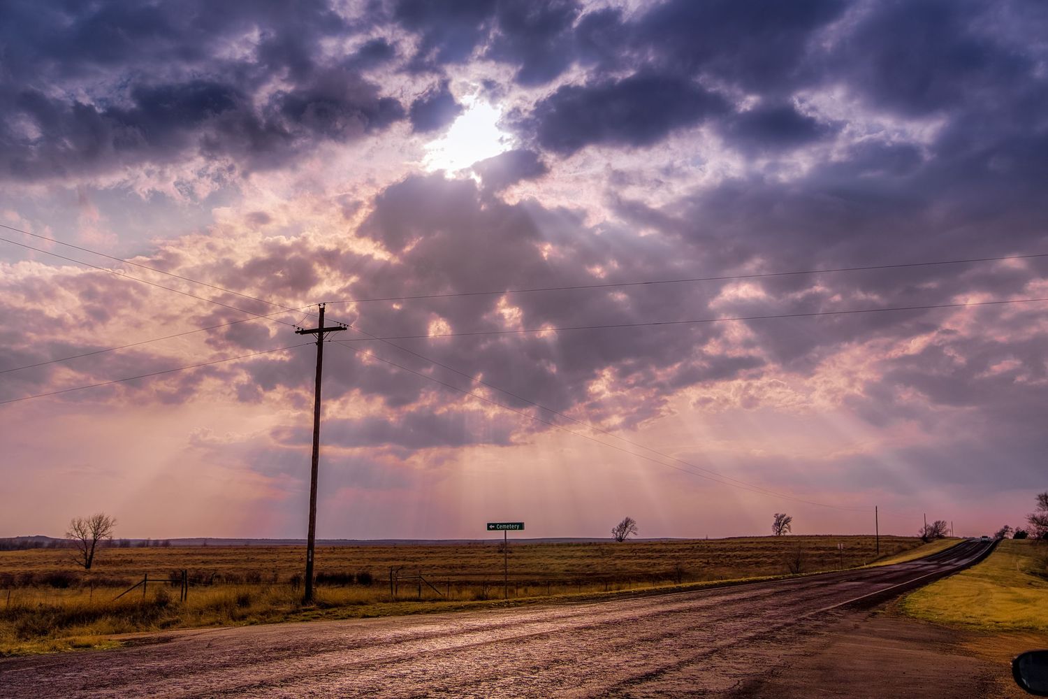 Sun rays break through stormy clouds over a rural road at golden hour.