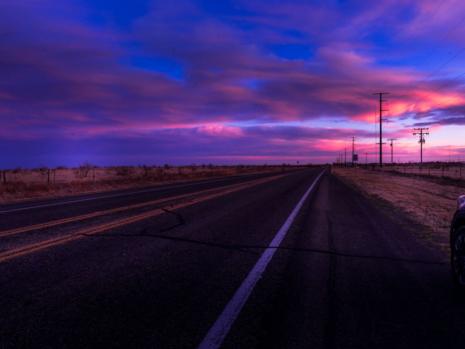 Empty rural road at dusk under dramatic purple and pink cloudy sunset sky.