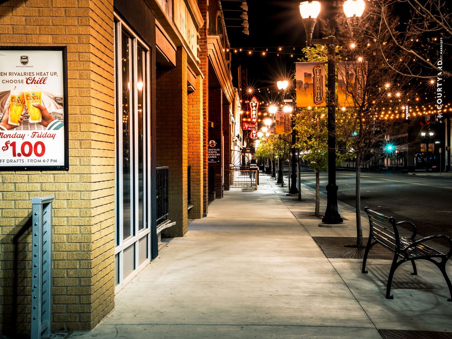 Night photo of a brick sidewalk with string lights, benches, and a Sonic restaurant advertisement sign.