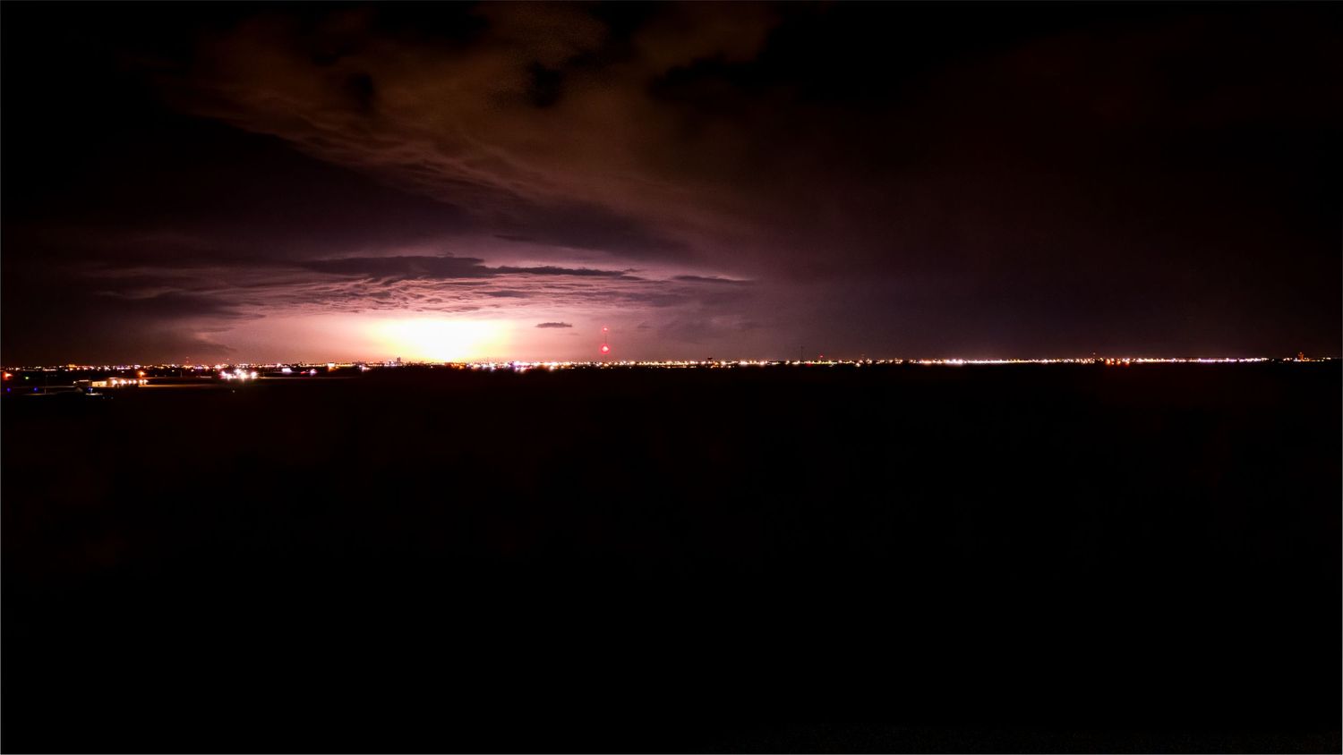 Dark panoramic night sky with distant city lights glowing on the horizon.