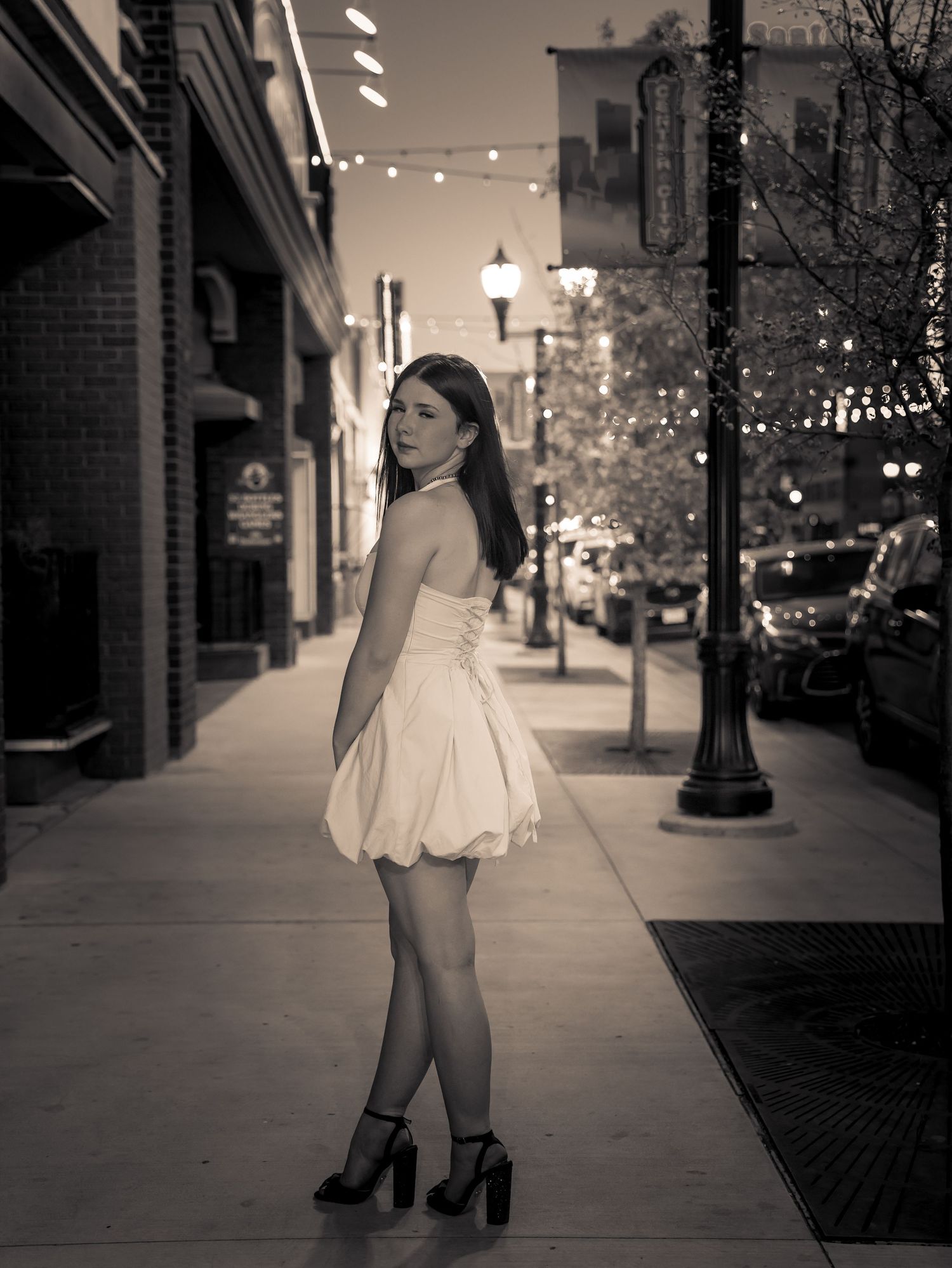 Black and white photo of woman in white dress on city street at night.