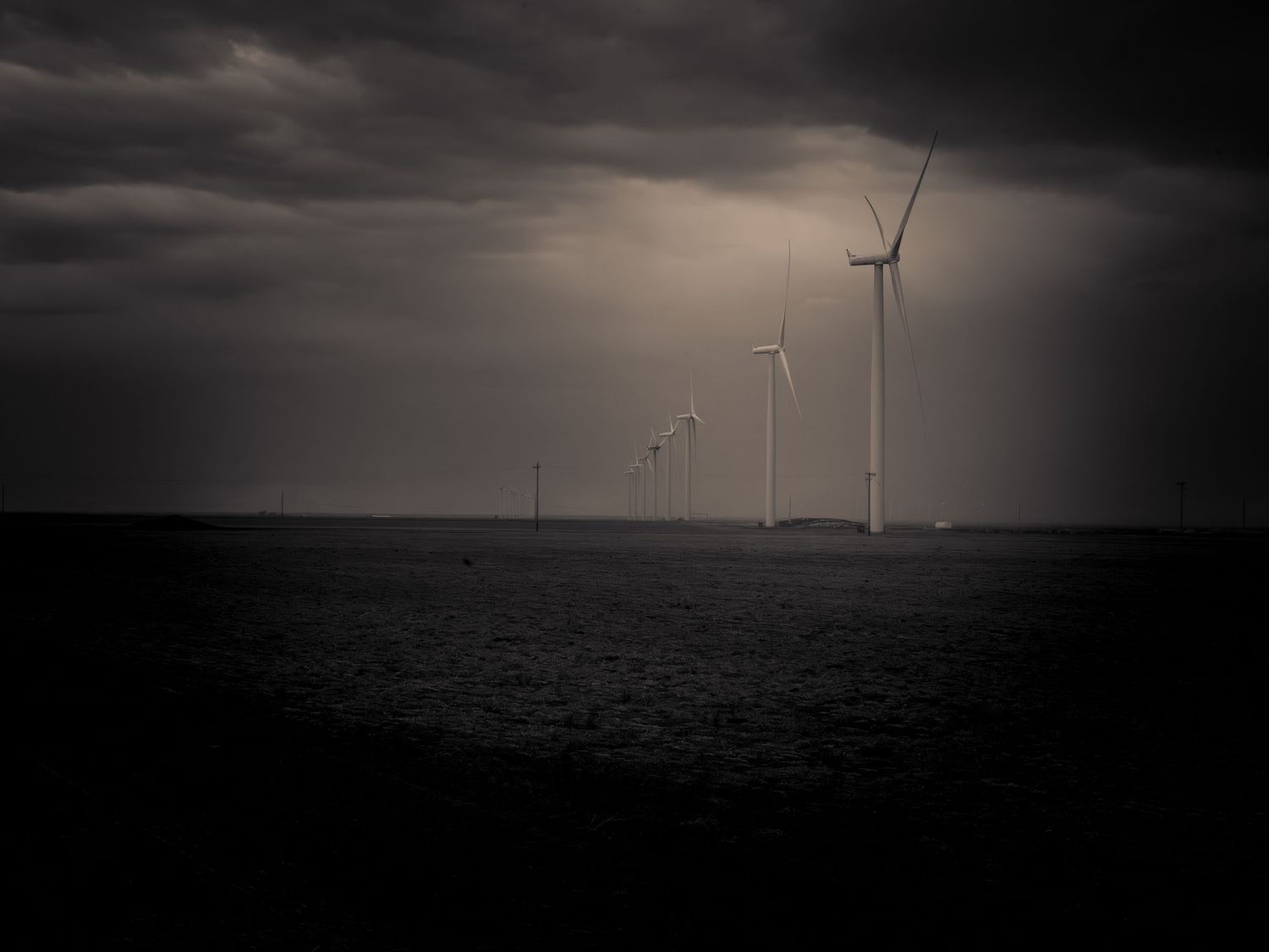 Dramatic dark moody offshore wind turbines standing in stormy sea under cloudy skies.