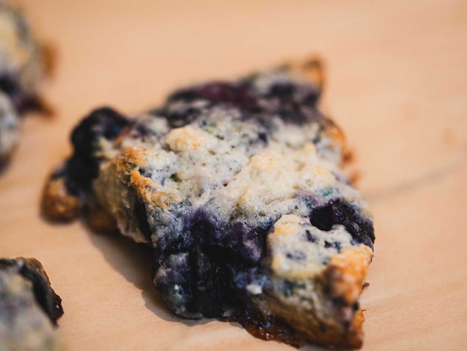 Close-up of a freshly baked blueberry scone on a wooden surface, golden brown with juicy blueberries.