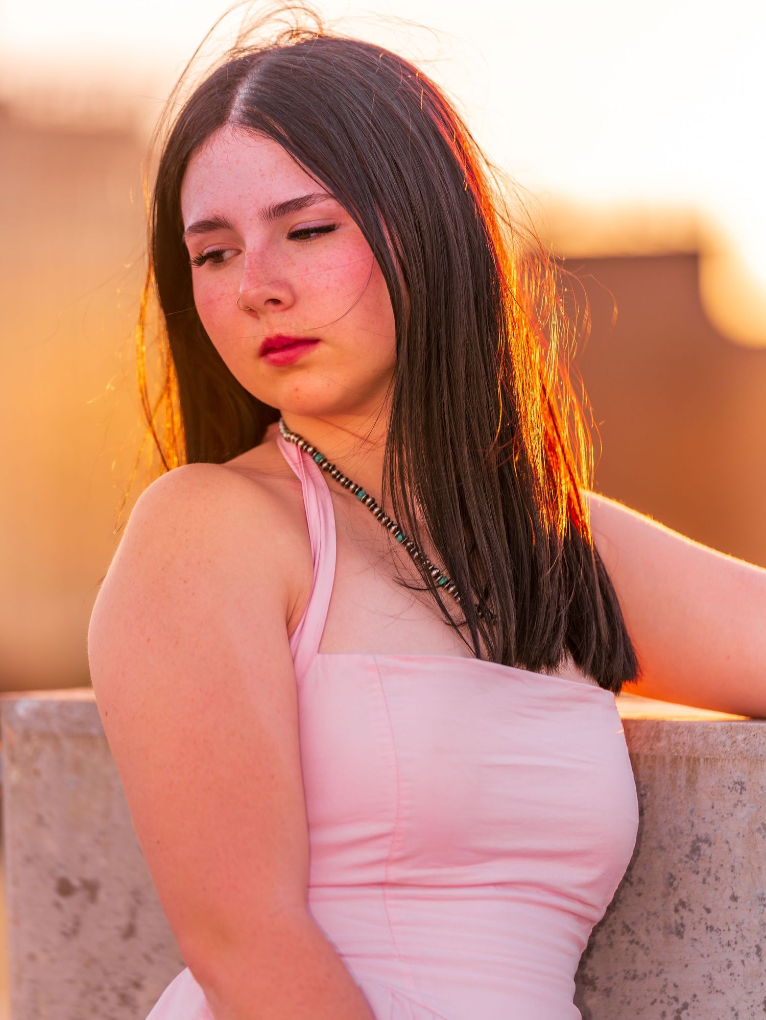 Young woman with dark hair in pink dress poses at golden hour sunset.
