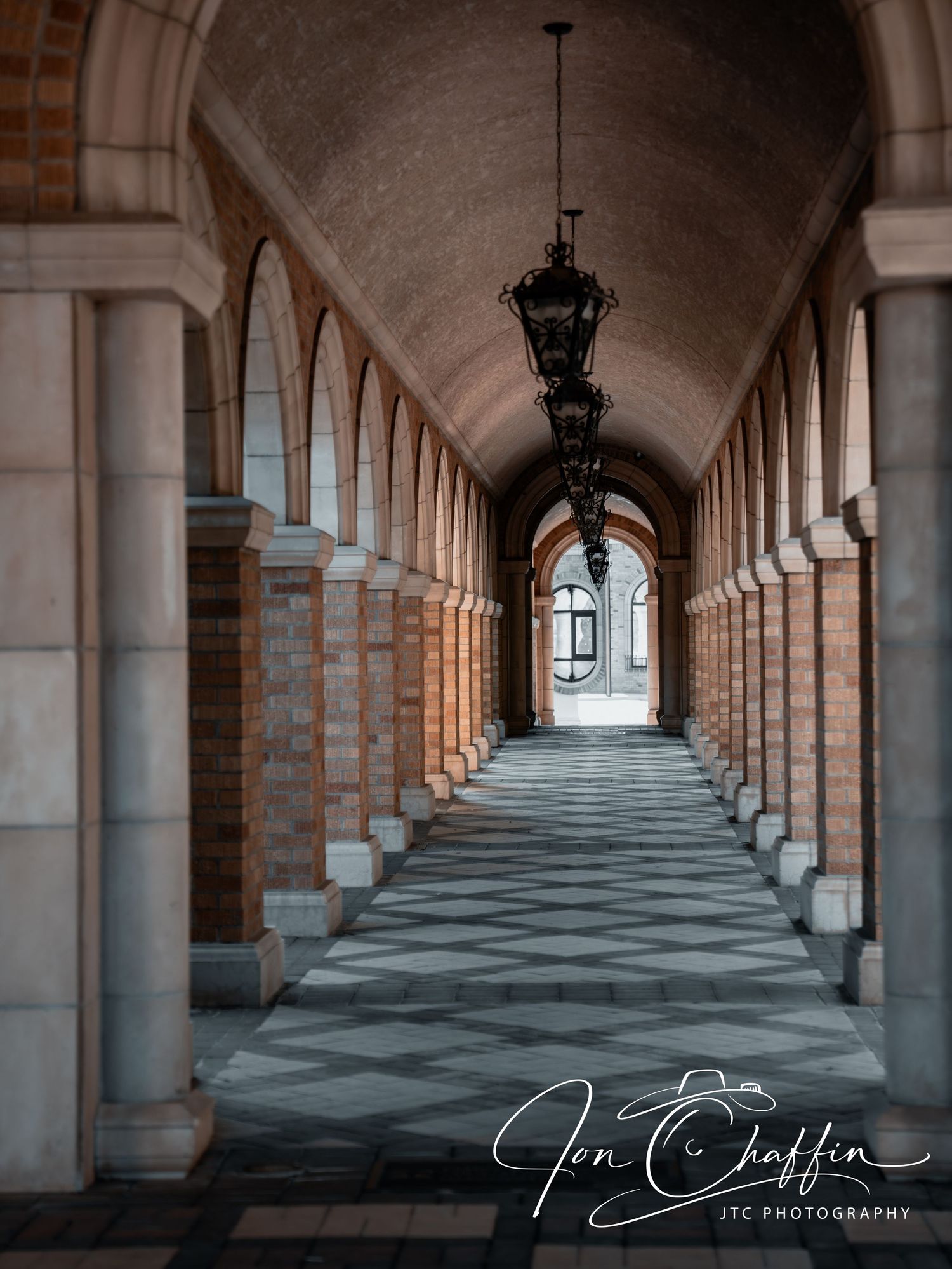 Elegant arched stone corridor with hanging lanterns and checkered tile floor.