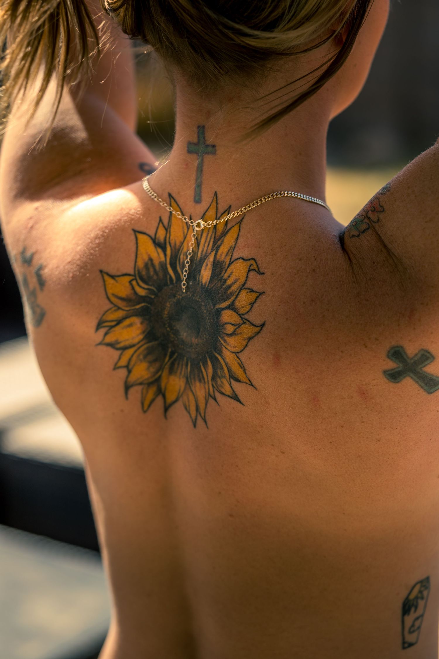 Colorful sunflower back tattoo with multiple cross tattoos in warm light.