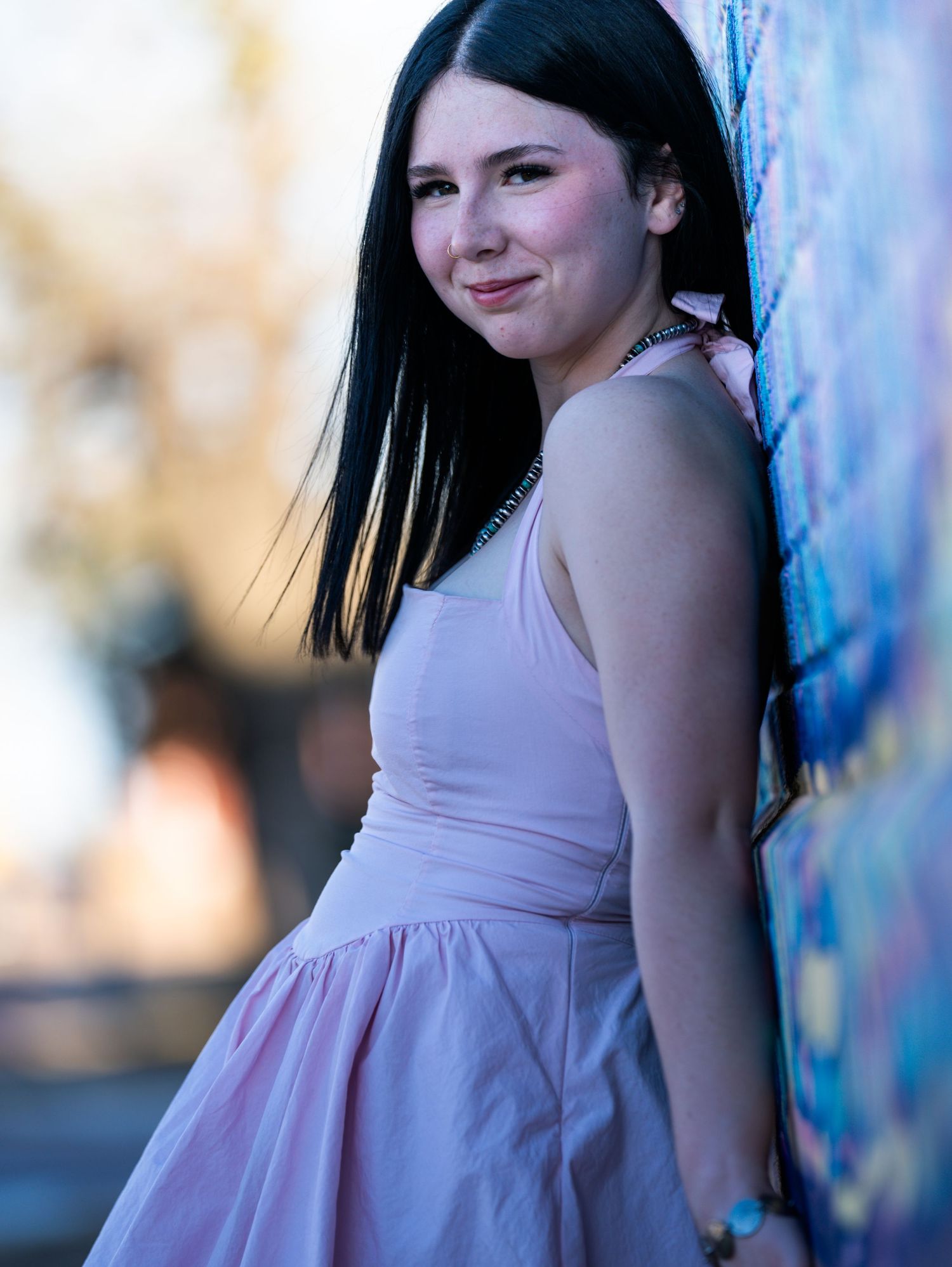 Smiling young woman in pink dress posing against vibrant mural wall.