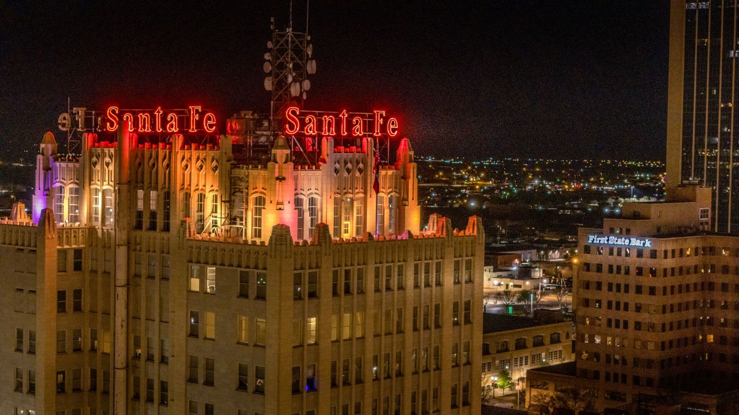 Night aerial photo of the Santa Fe building rooftop featuring bold red neon signs and richly lit architectural details.