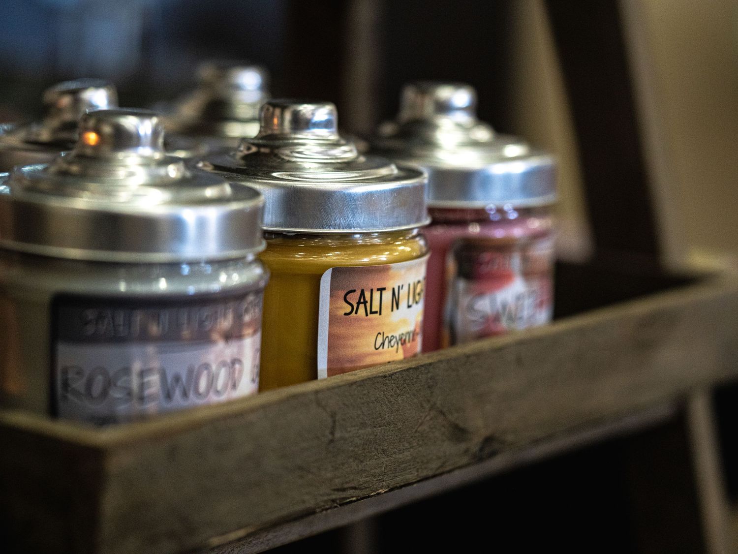 Rustic wooden tray displaying Salt N Us seasoning jars with silver lids, including Rosewood and Orange flavors.