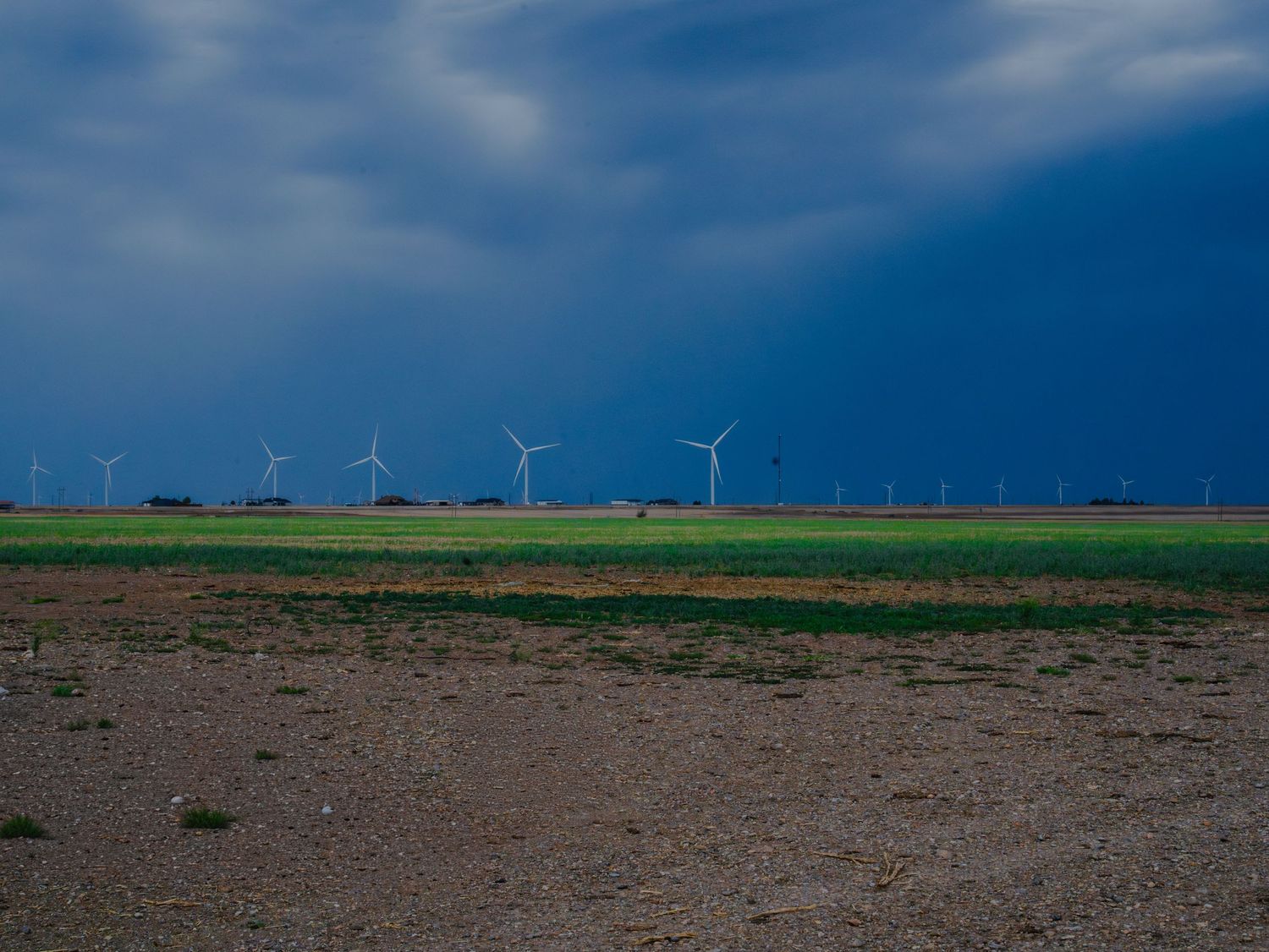 Wind turbines on green plains under dramatic dark storm clouds in rural landscape.