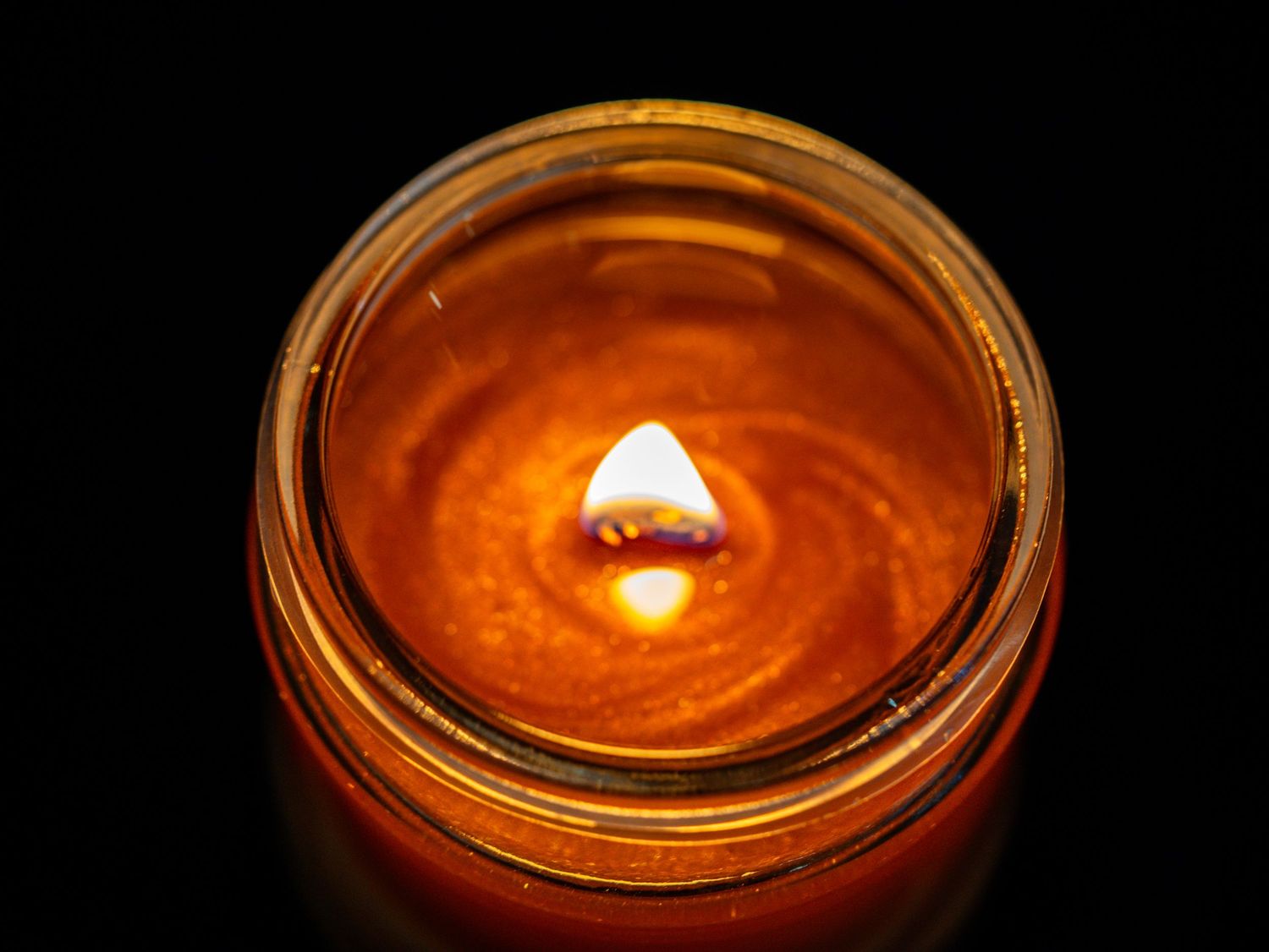 A glowing amber candle burning in a glass jar against a dark black background.