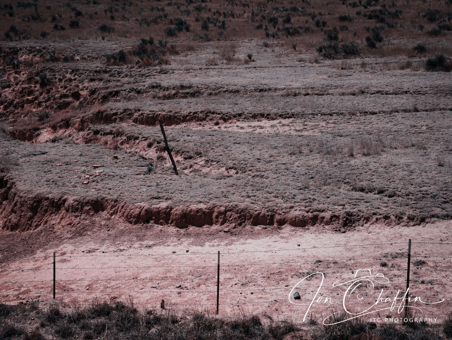 Aerial view of eroded red dirt terrain with fence posts in arid Texas landscape.