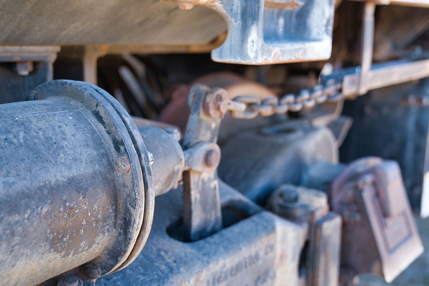 Close-up of worn rusty train undercarriage components with chains and metal fittings.