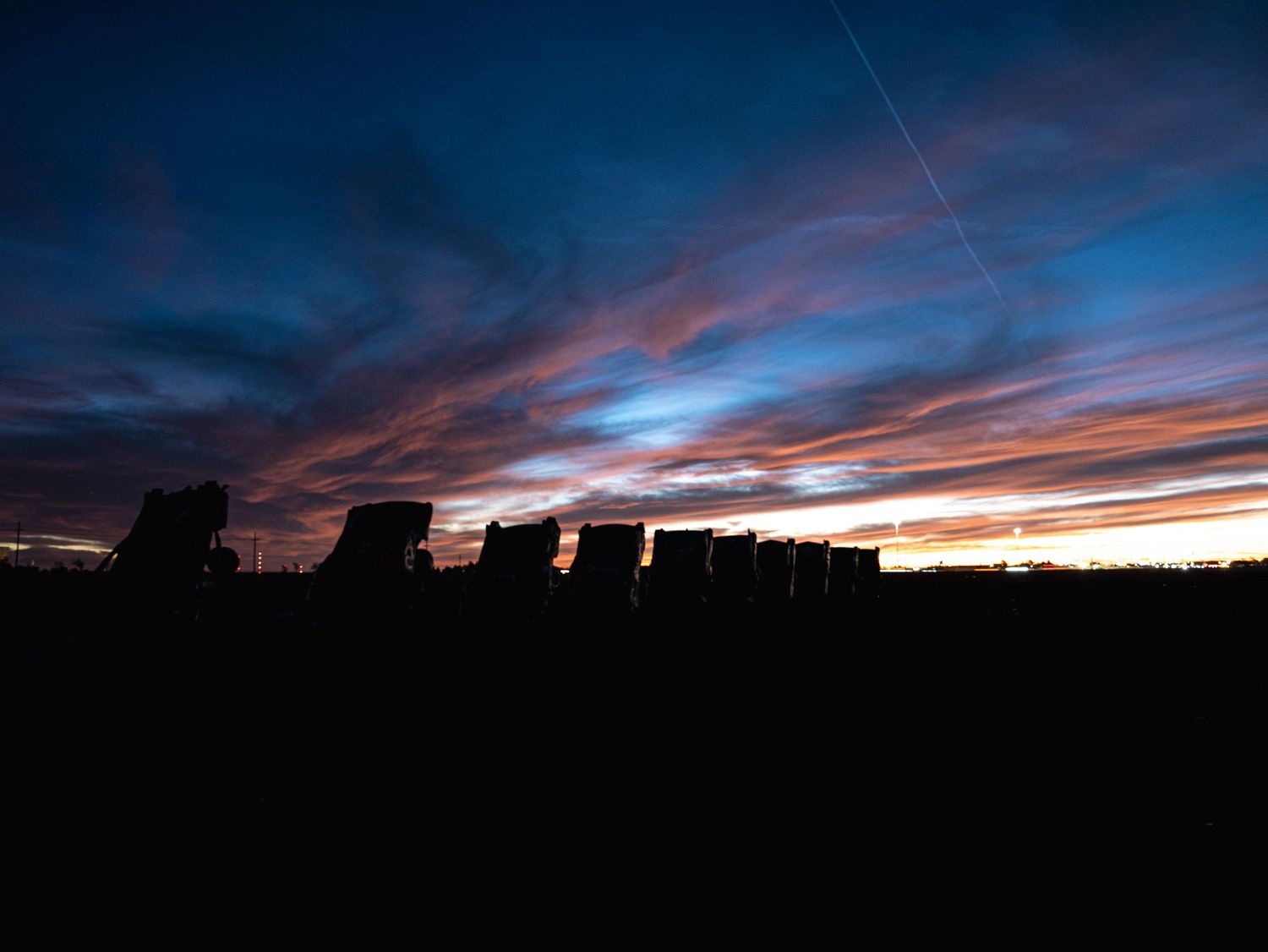 Striking blue and orange sunset sky behind the dark silhouettes of buried cars at Cadillac Ranch, Texas.
