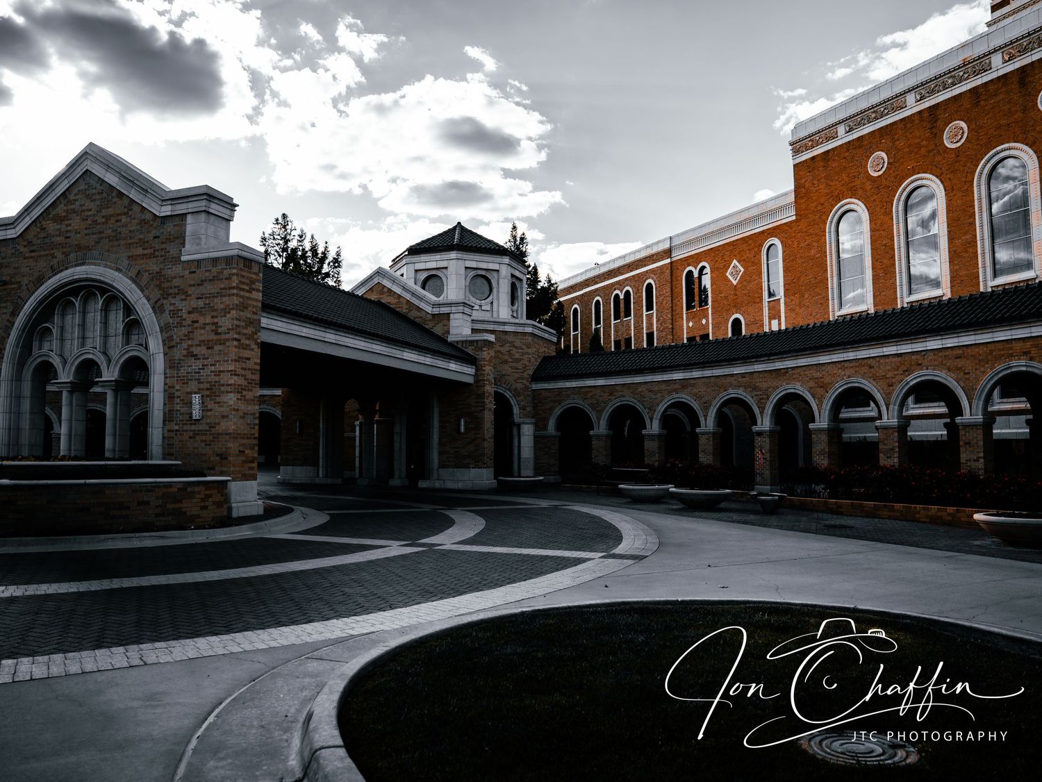 Elegant brick courtyard of a historic building with arched walkways under dramatic cloudy sky.
