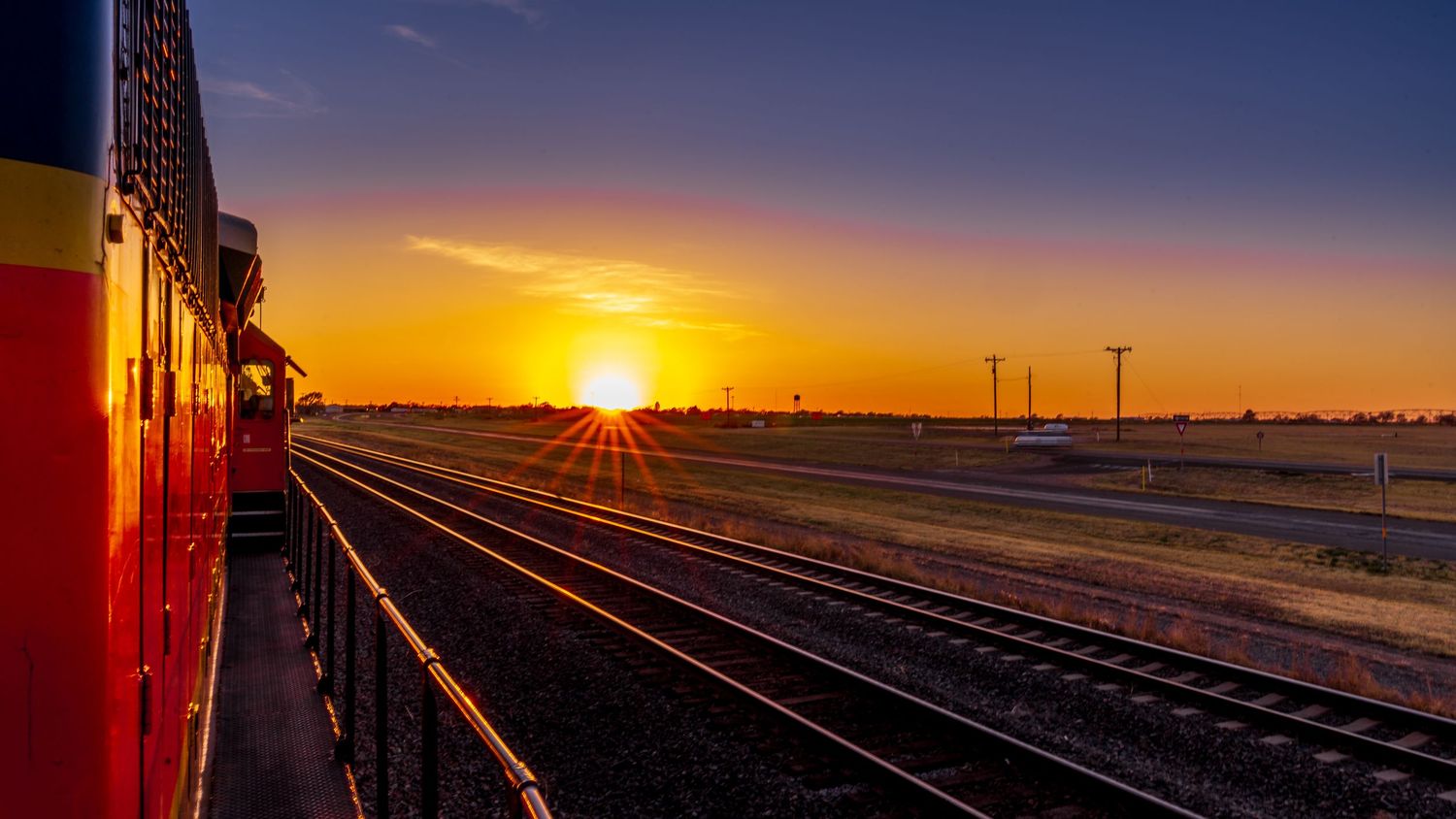Colorful train alongside railway tracks during stunning golden sunrise.
