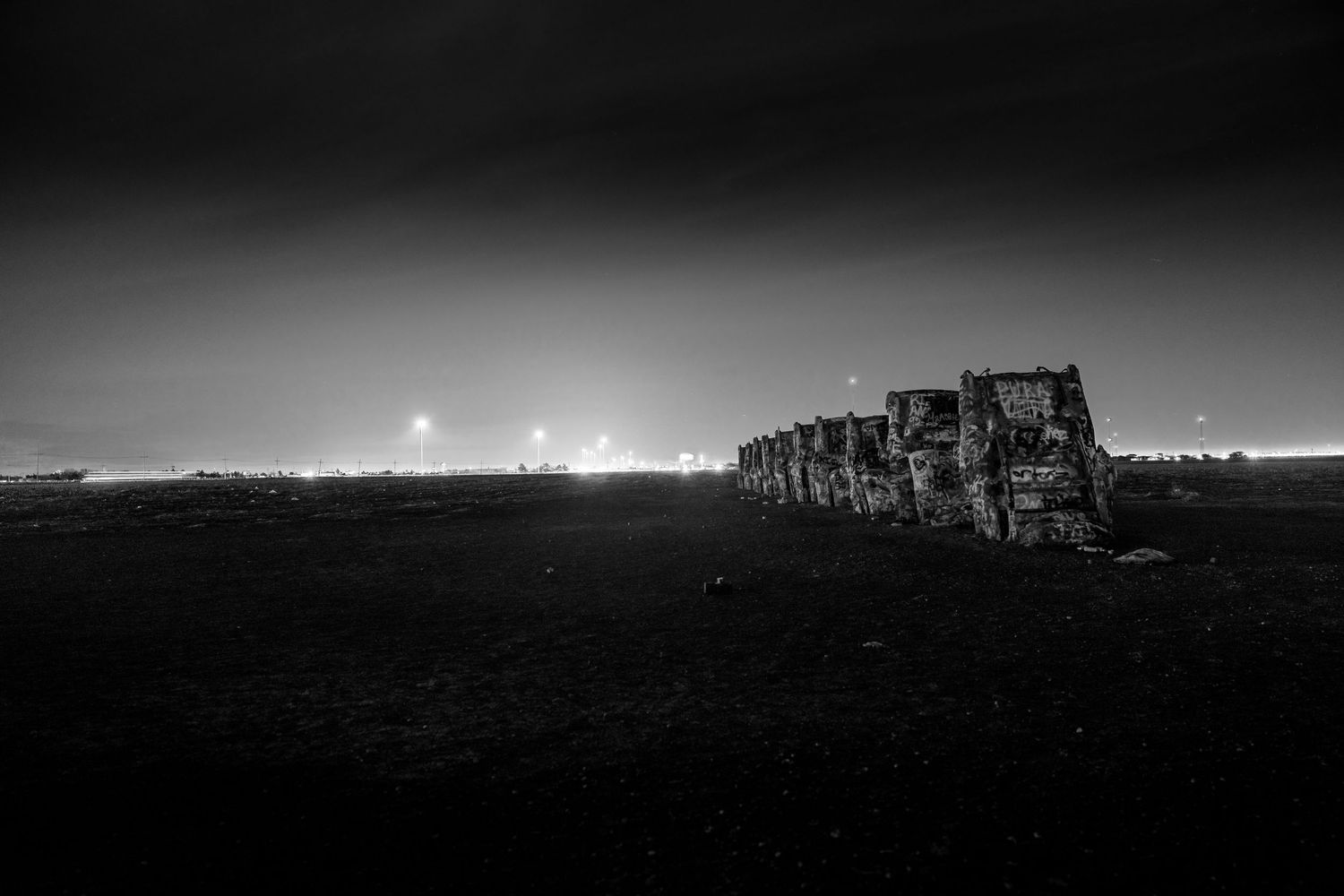 Black and white photo of Cadillac Ranch installation under dramatic night sky.