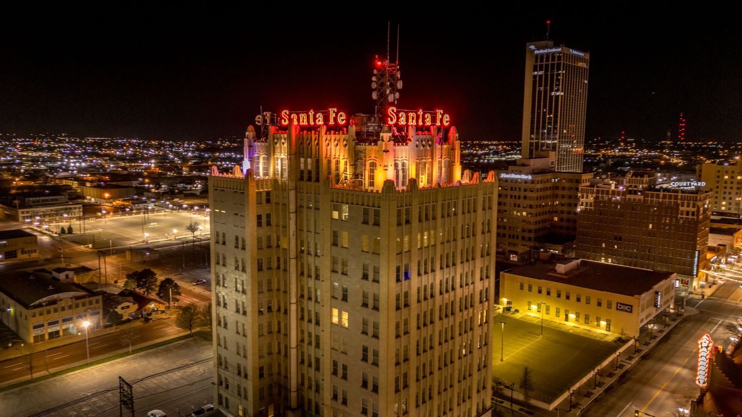 Close-up aerial night shot of the ornate Santa Fe building rooftop with vivid red neon signs and colorful lighting.