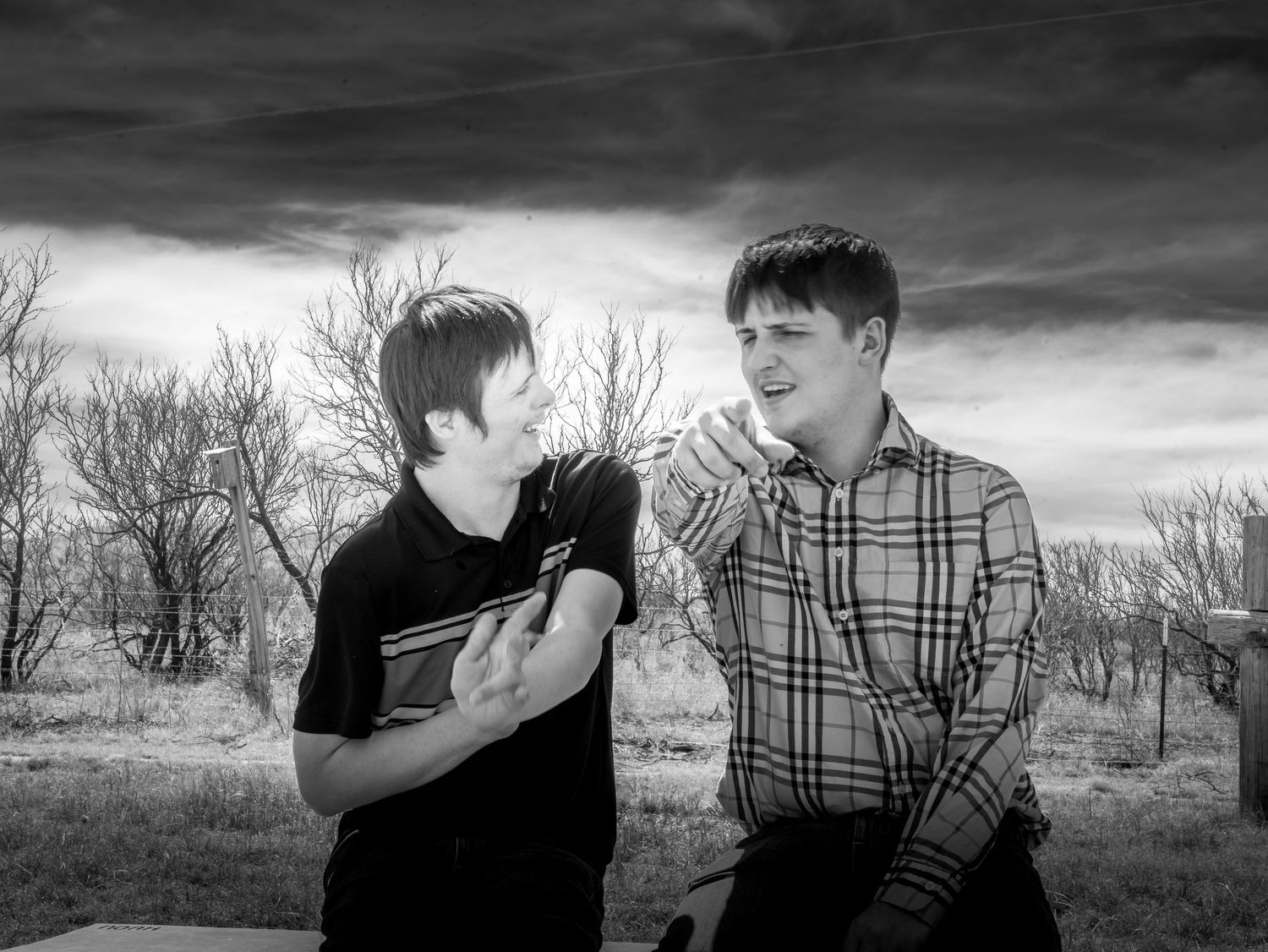 Black and white photo of two young men sharing a lighthearted moment outdoors among bare winter trees.