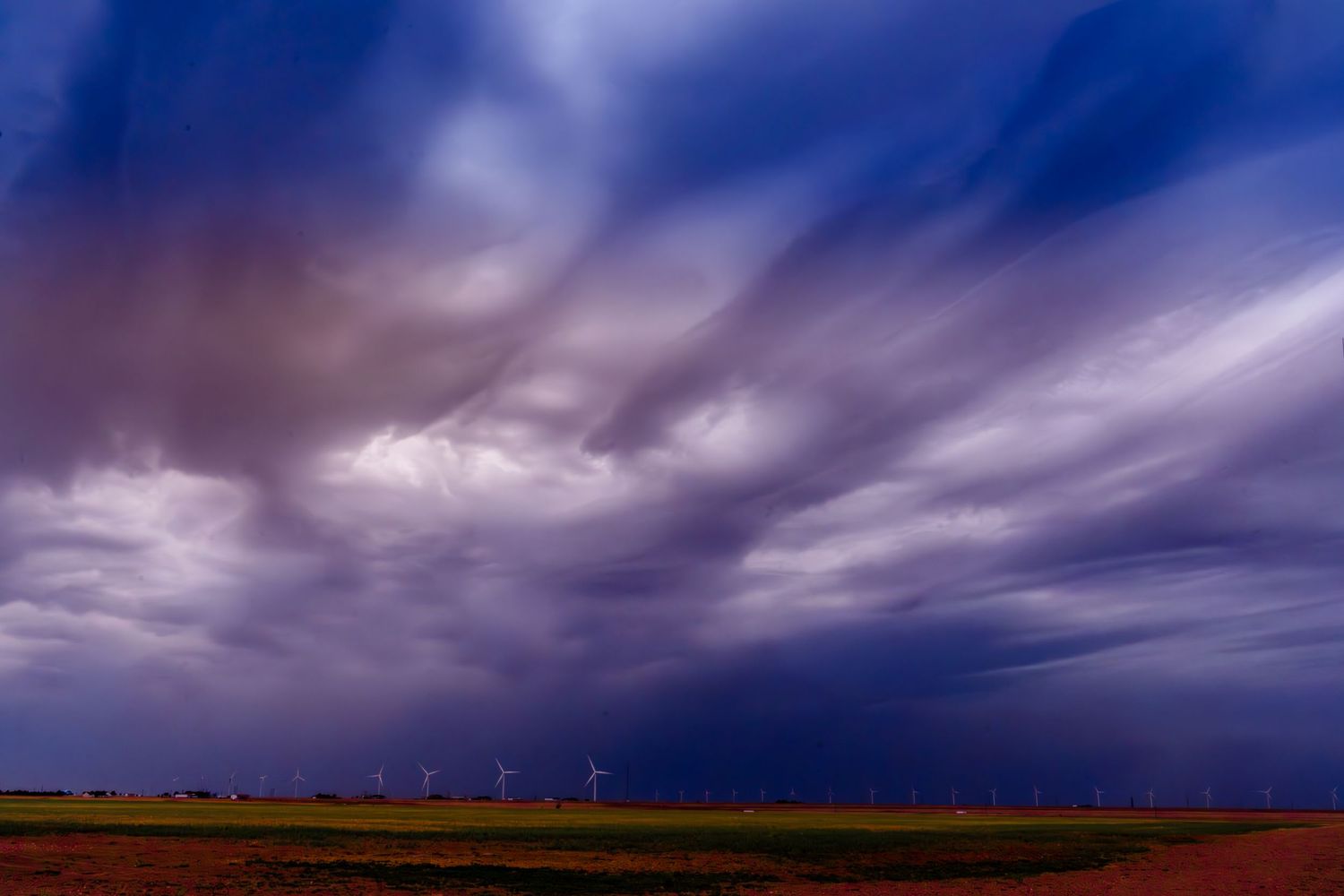 Dramatic storm clouds swirl over a wind farm on the Great Plains at dusk.