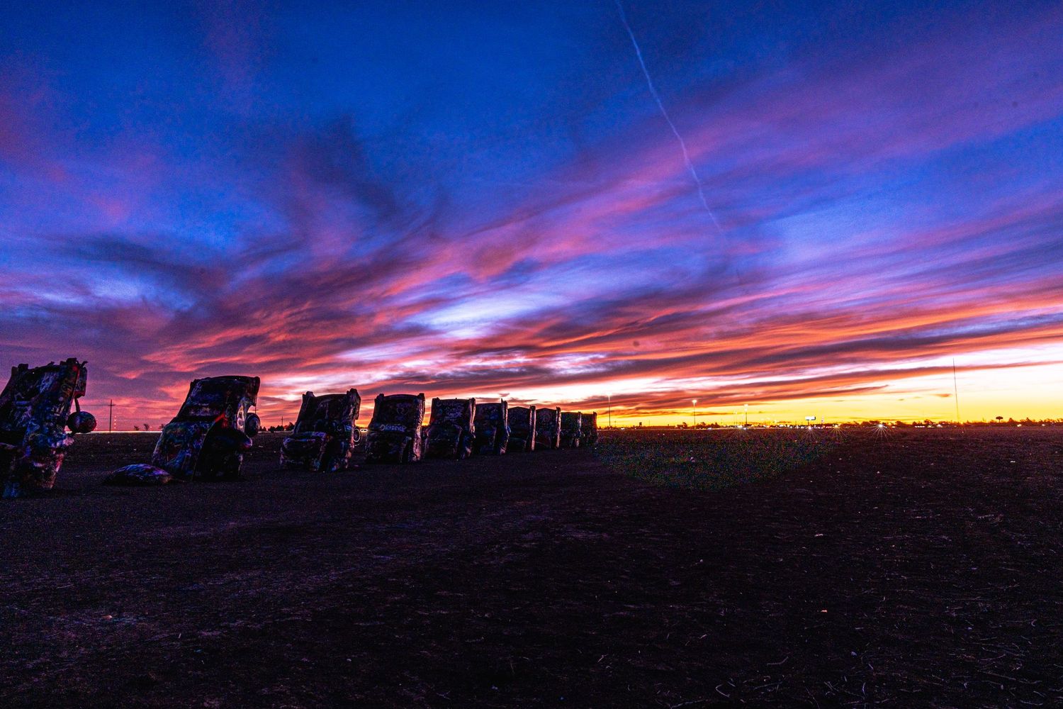 Vivid red and blue sunset sky illuminates the silhouetted row of buried Cadillacs at Cadillac Ranch, Texas.