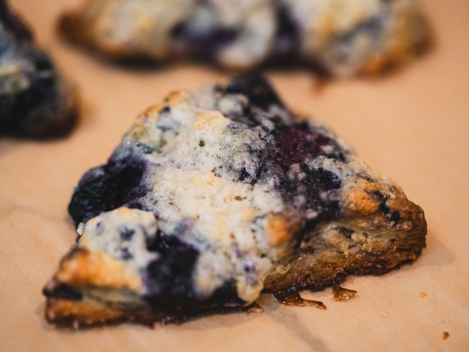 Close-up of a fresh blueberry scone with sugar topping on parchment paper, perfect for bakery menus.
