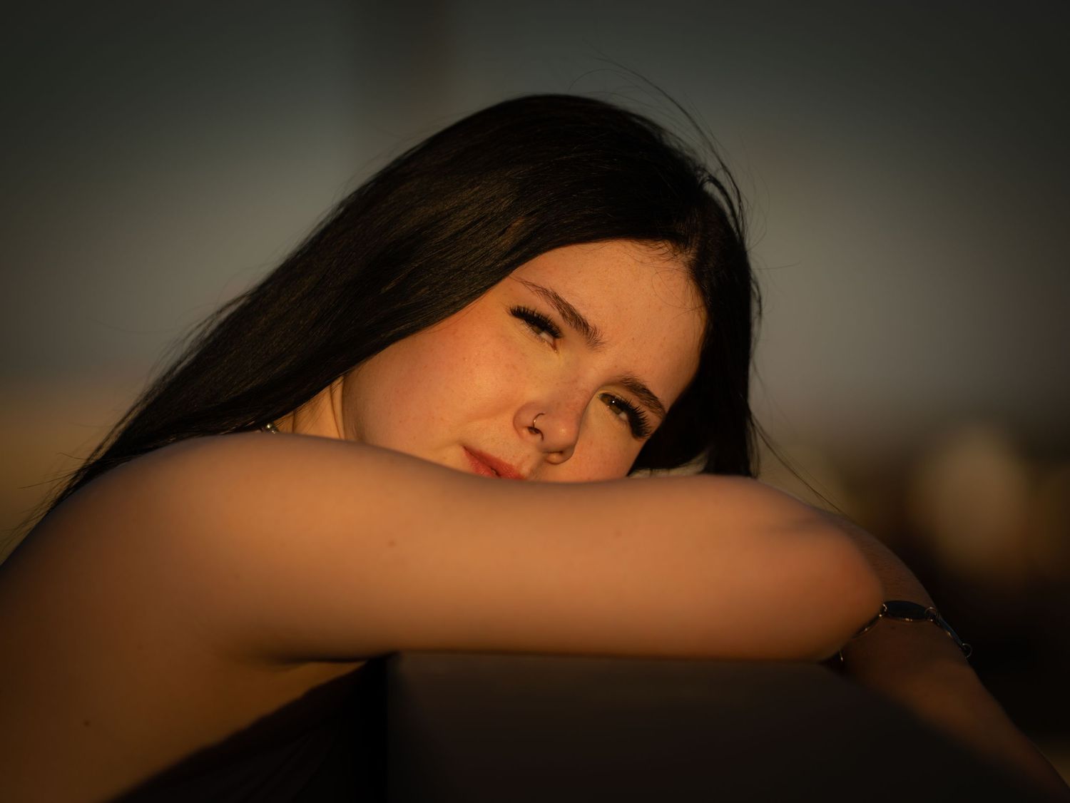 Close-up portrait of young woman resting head on arms in warm golden hour light.