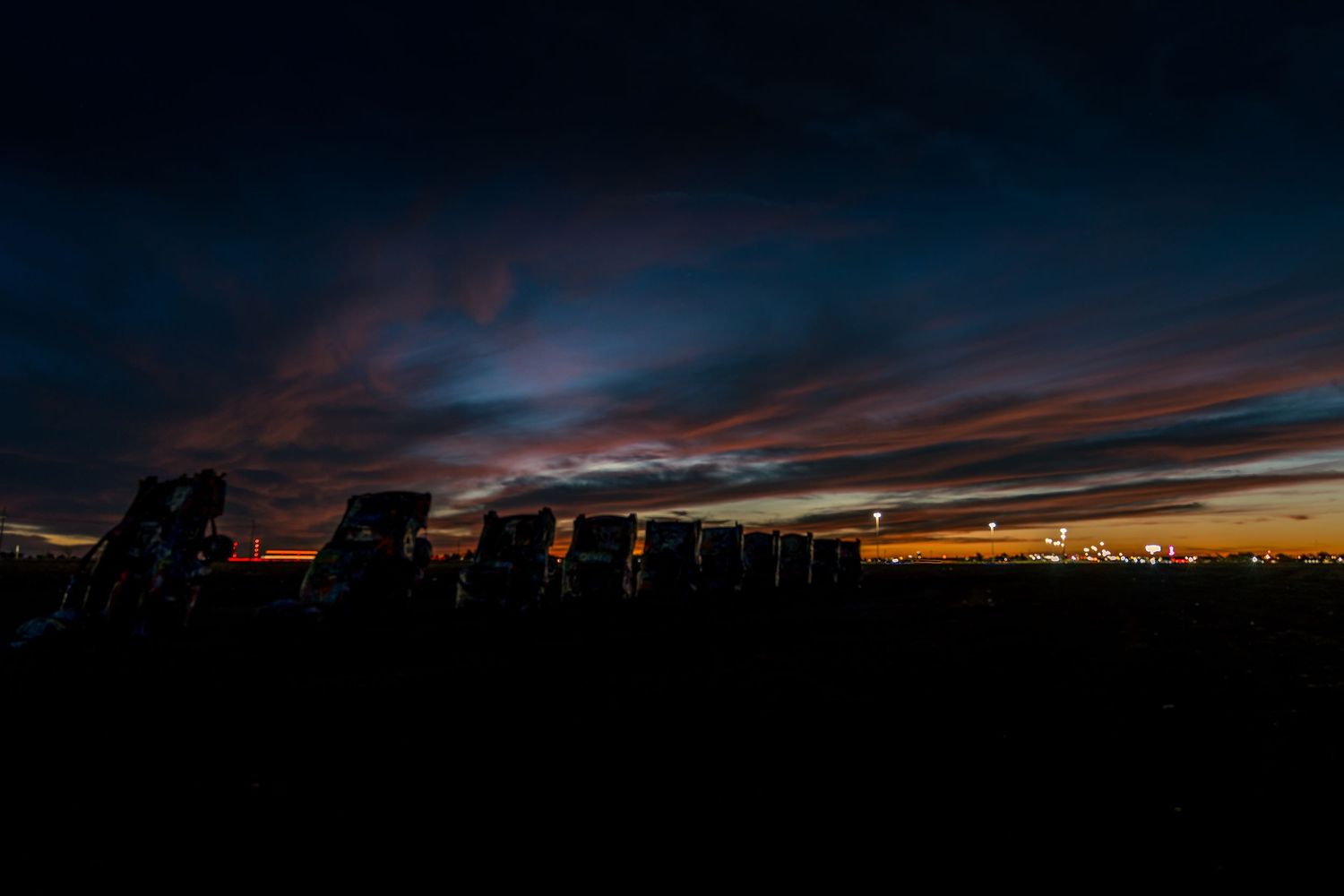 Dark silhouettes of buried Cadillacs at Cadillac Ranch beneath a vivid blue and orange sunset sky in Amarillo.