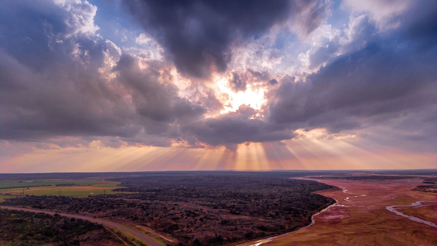 Dramatic sun rays piercing through storm clouds over a vast flat landscape.