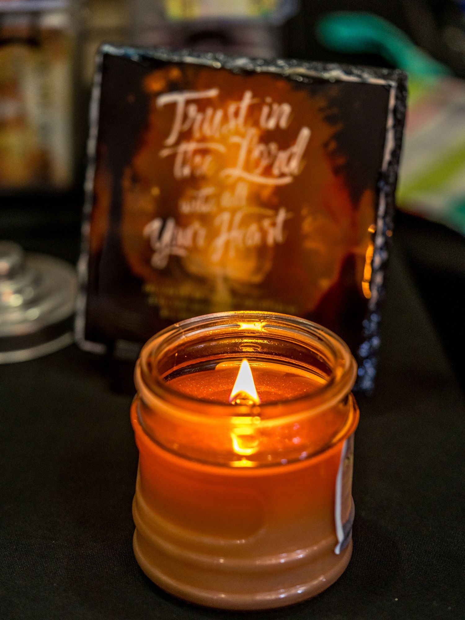 Lit amber candle in glass jar glowing warmly beside a decorative slate sign reading Trust in the Lord with all Your Heart.