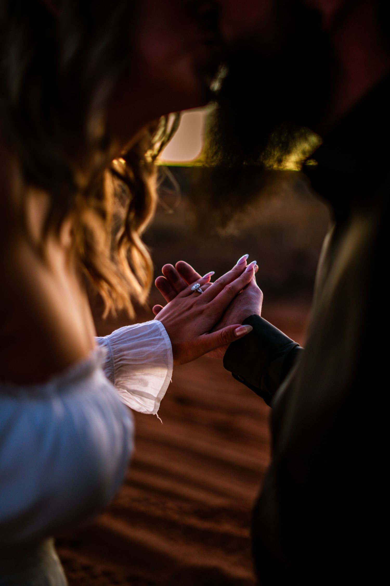 Romantic couple holding hands with engagement ring visible during a warm sunset ceremony.