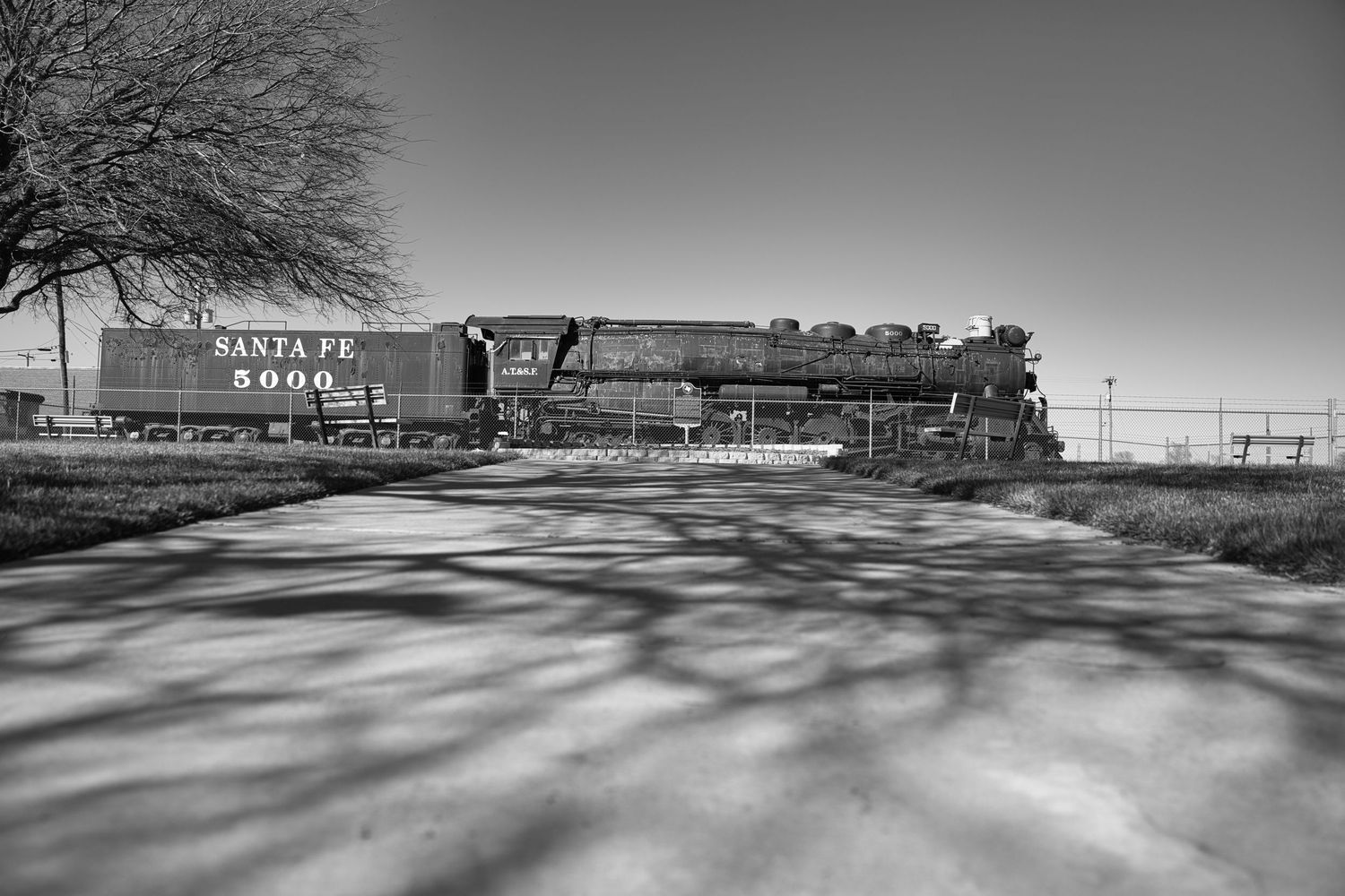 Black and white photo of Santa Fe 5000 steam locomotive with tree shadows on pavement.