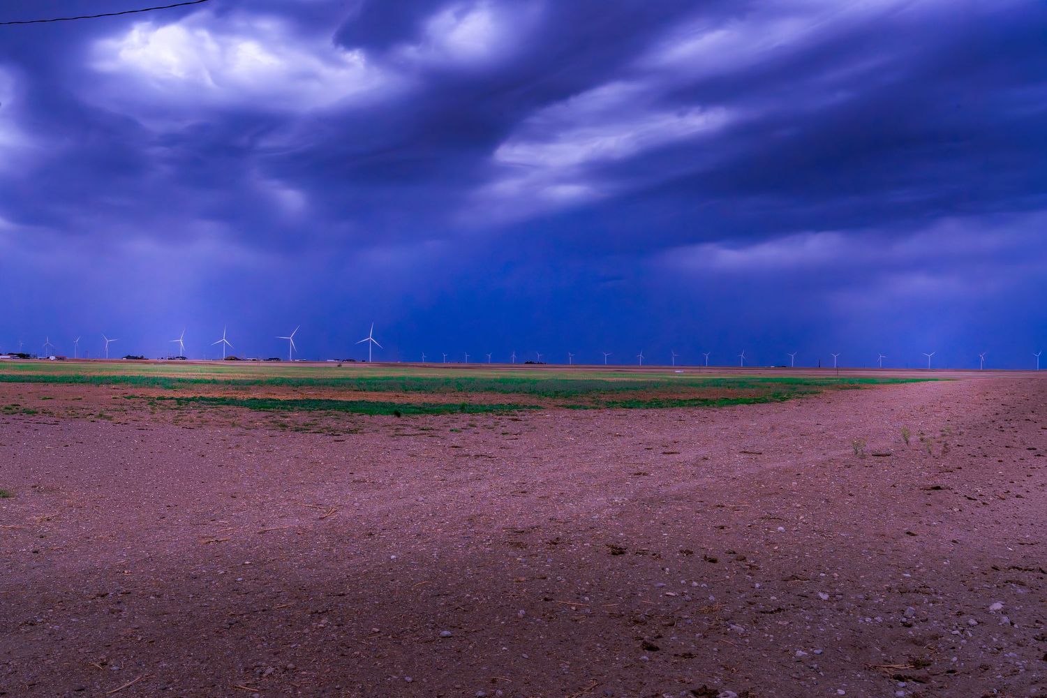 Stormy blue twilight sky over flat farmland with distant wind turbines.