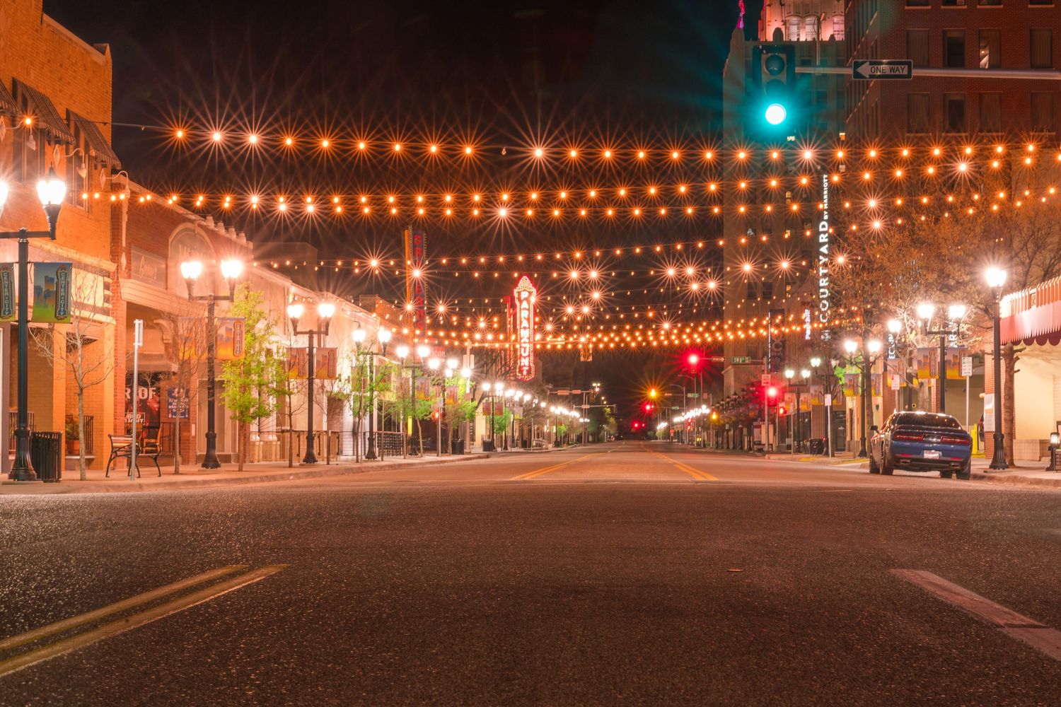 Night view of a city street decorated with warm string lights and traffic signals on Santa Fe Avenue.