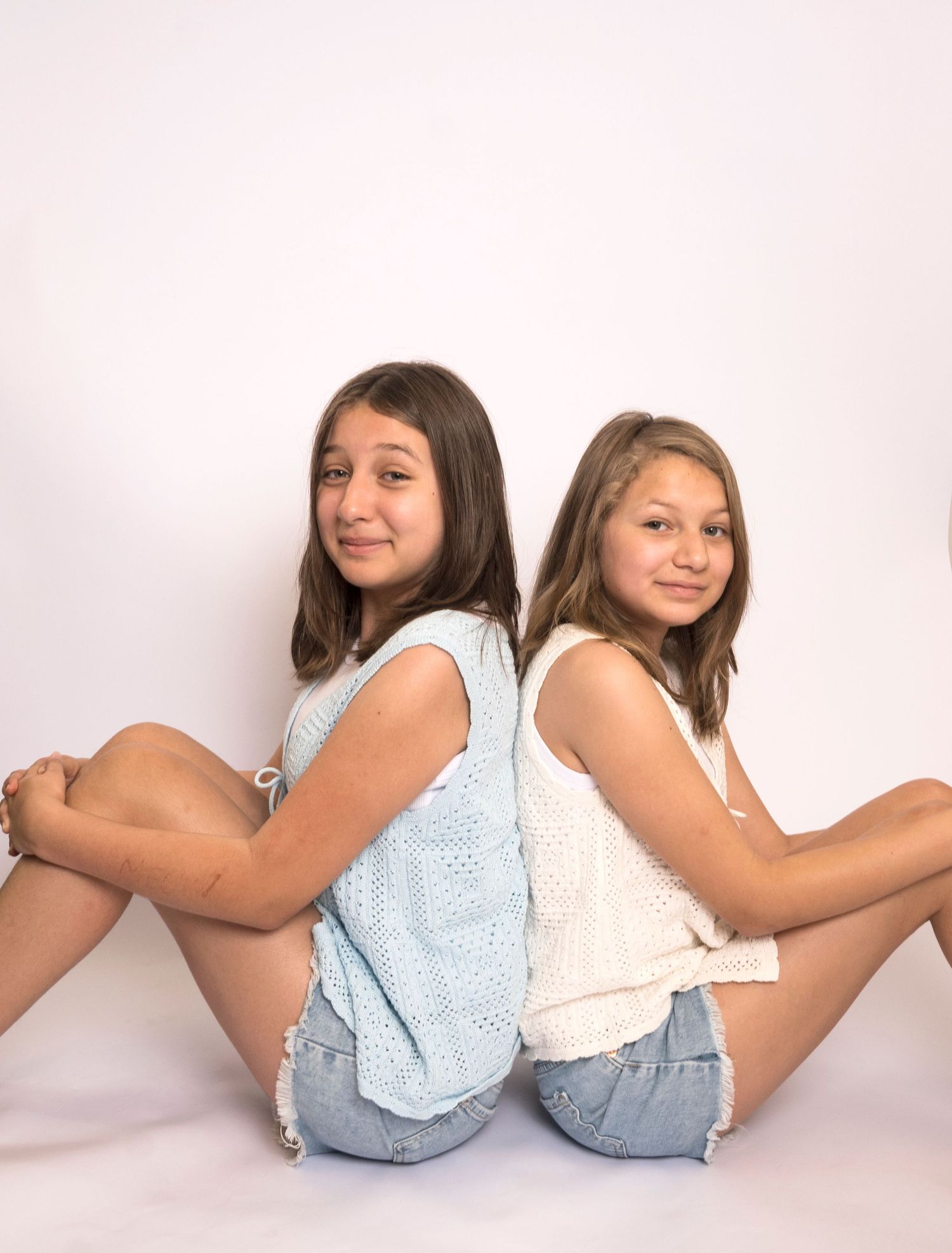 Two sisters sitting back-to-back and smiling during a studio sibling portrait by a Central Florida Photographer.