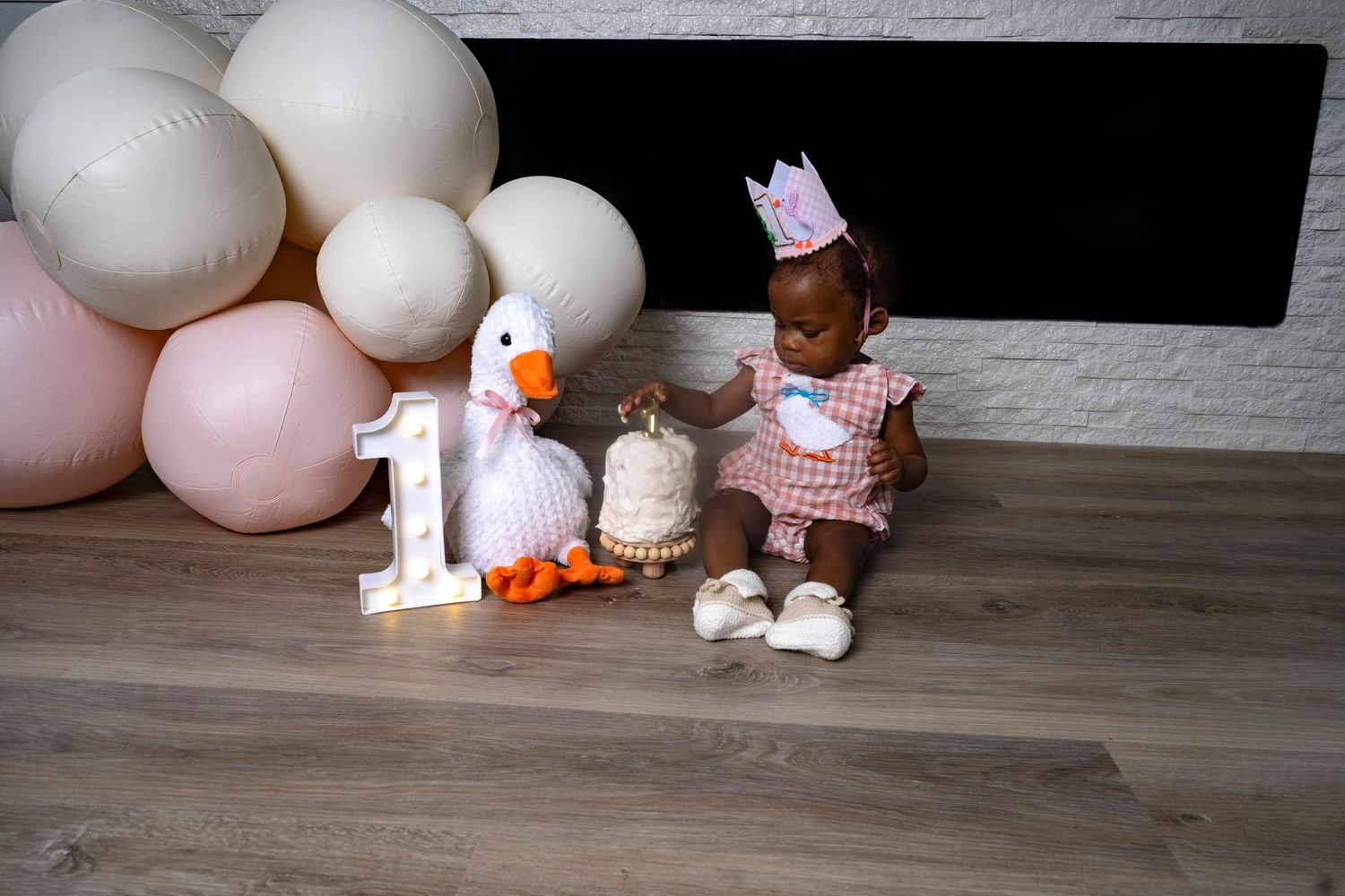 One-year-old girl sitting with pastel balloons and birthday decor during a milestone session by a Central Florida Photographer.