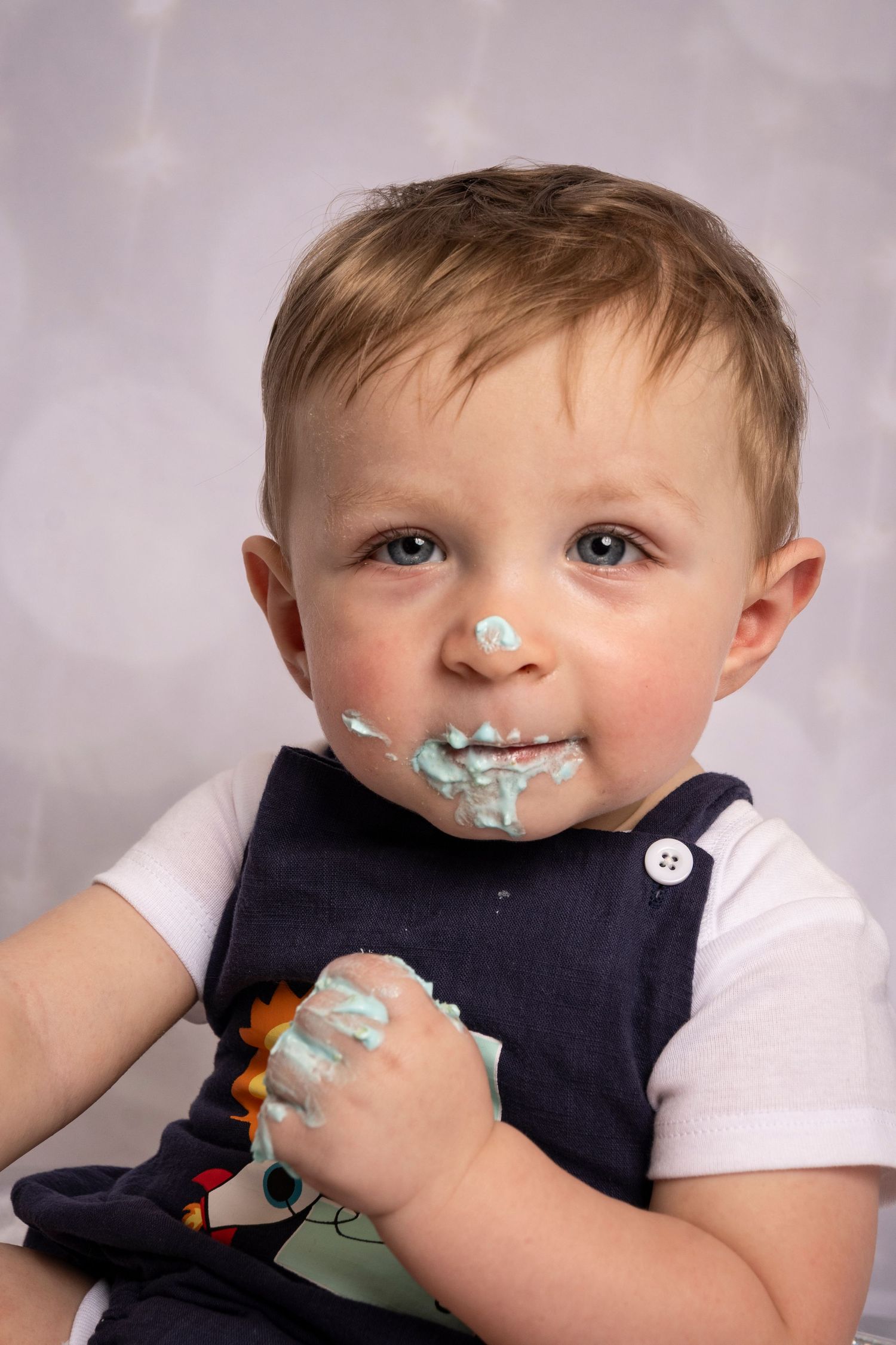 Smiling one-year-old with frosting-covered hands during a birthday cake smash by a Central Florida Photographer.