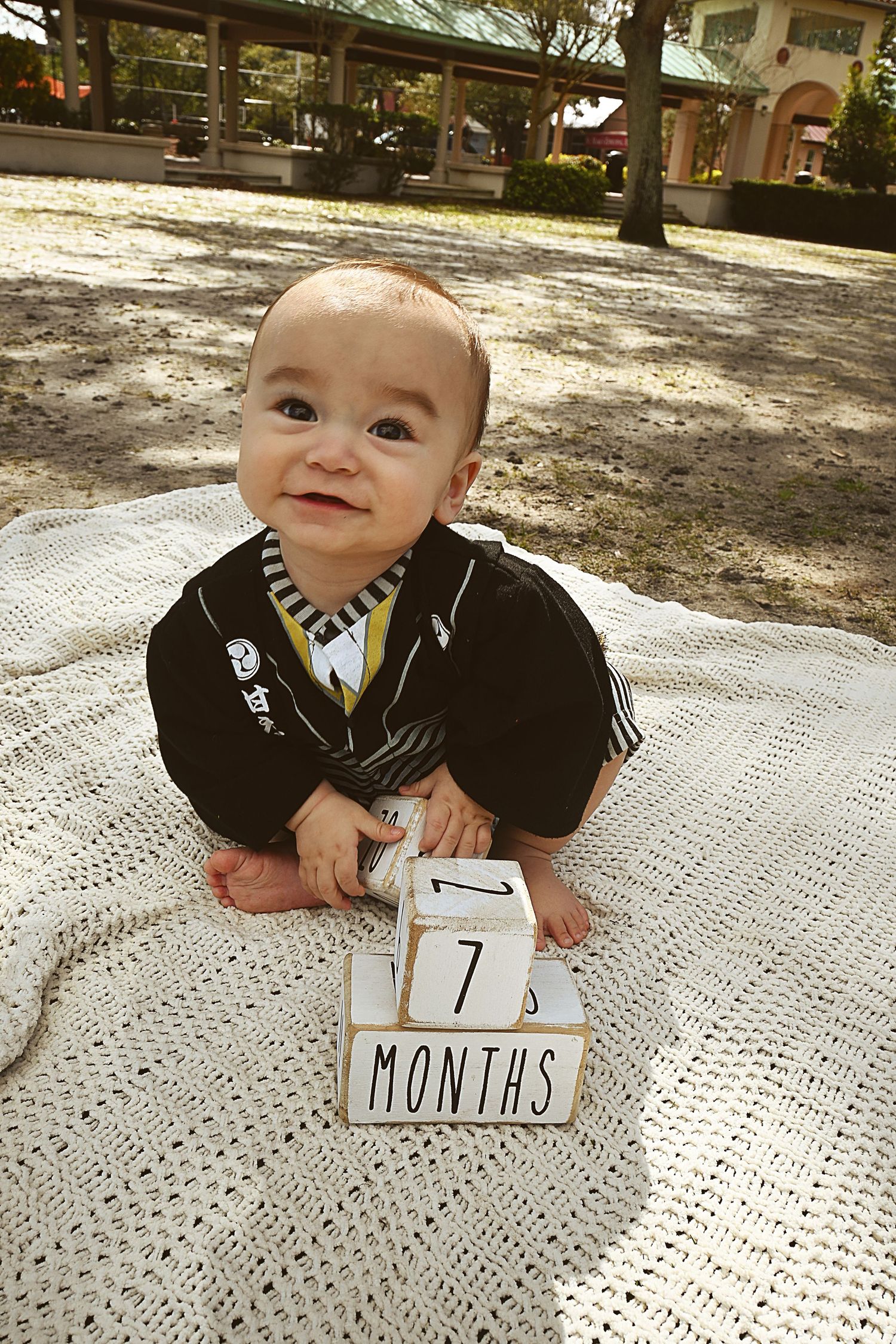 Smiling baby lying outdoors beside a number one block during a milestone session by a Central Florida Photographer.